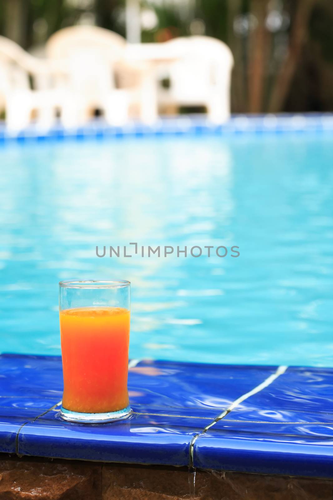 Closeup of orange juice glass standing on border of water pool