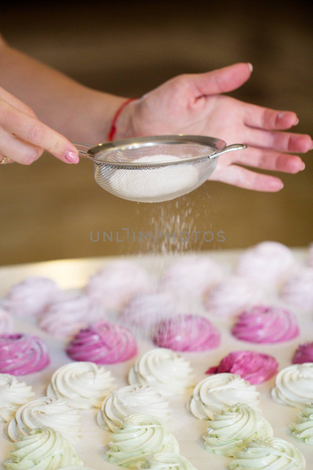 Woman's hands sprinkling with icing sugar a zephyr  using sieve. Confectioner sprinkles powdered sugar on marshmallow