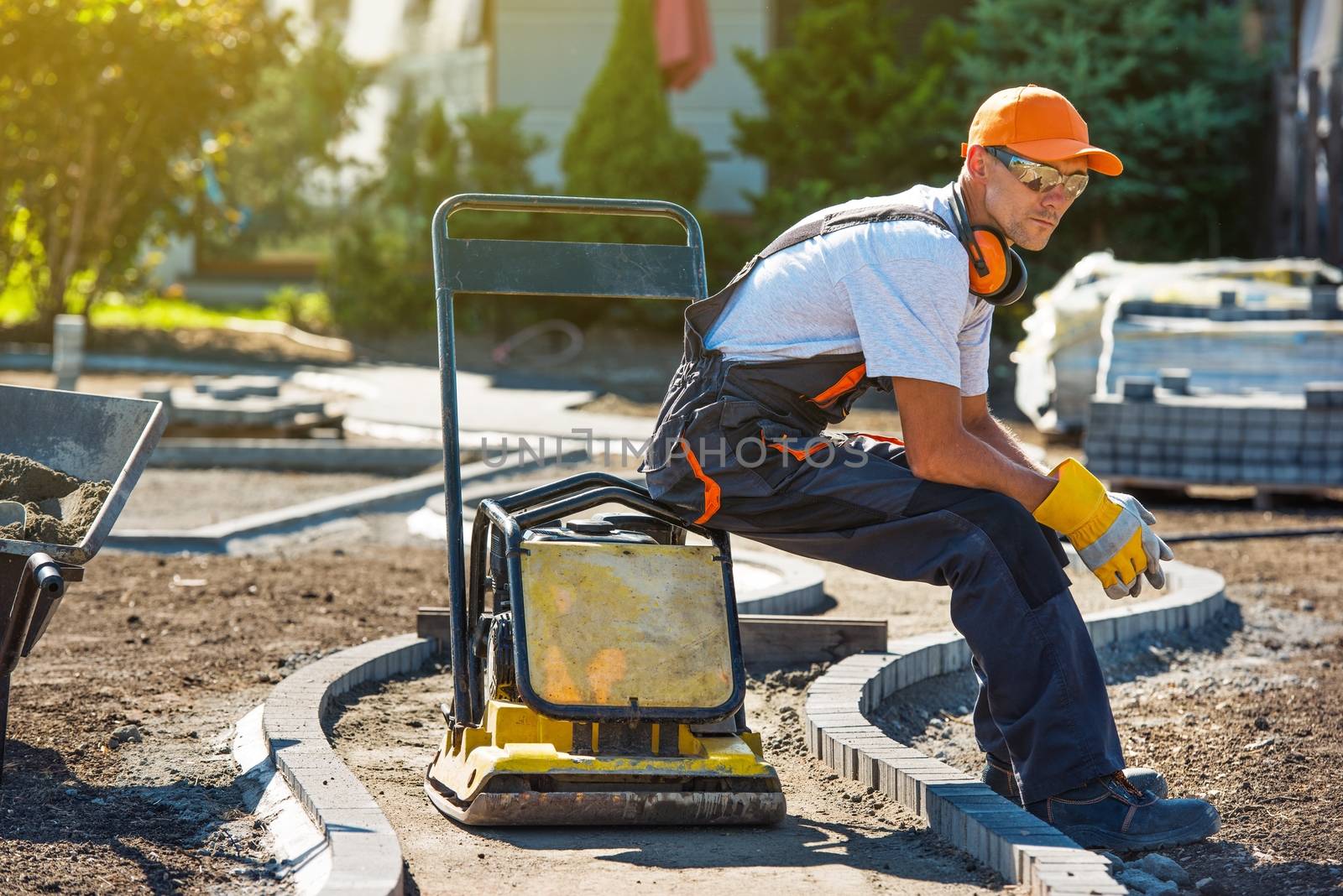 Brick Paver Worker Resting on His Soil Plate Compactor While at Work.