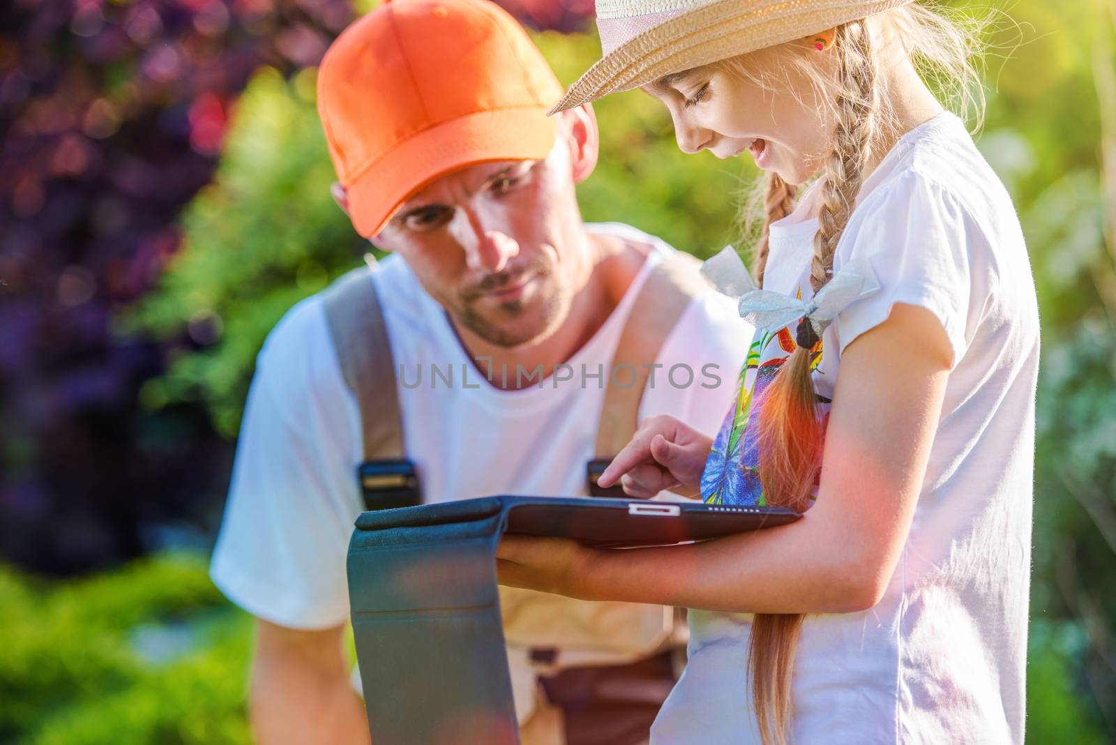 Family Time in the Garden. Girl Showing Her Dad How Internet Works While Playing on Her Tablet Device.