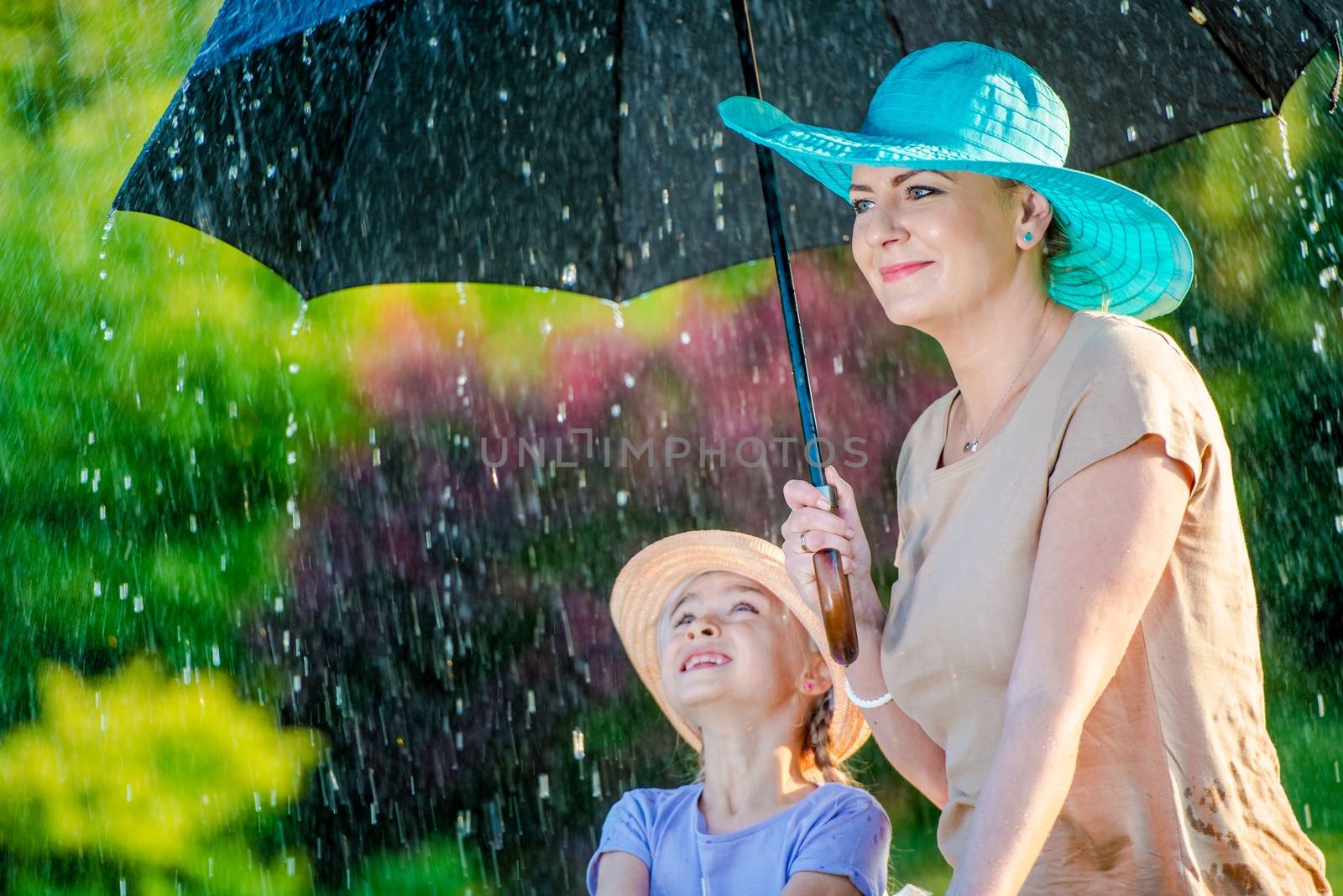 Caucasian Mother with Daughter Under Large Umbrella During Summer Rain.