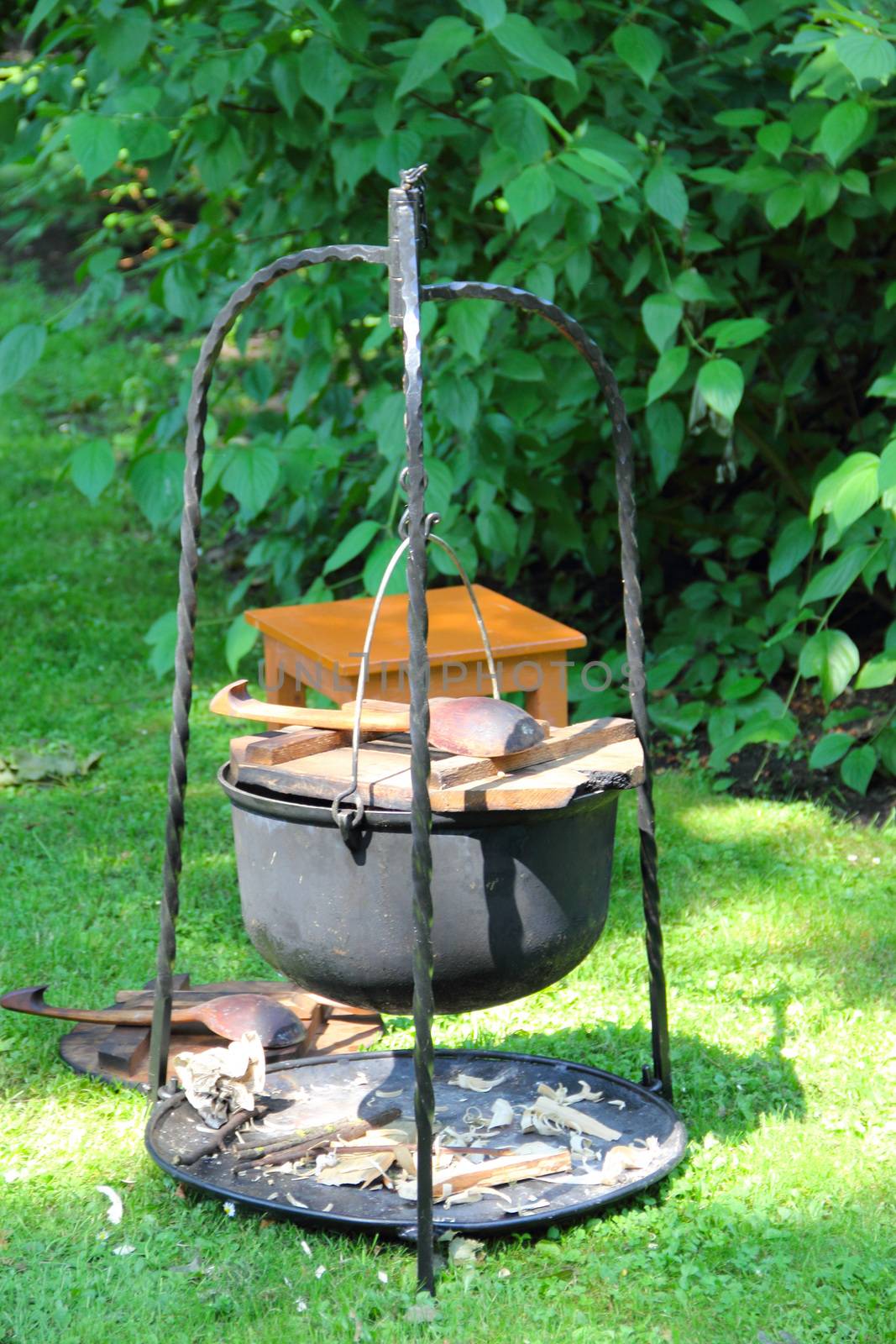 Witches black kettle and firewood on forged stand on green grass