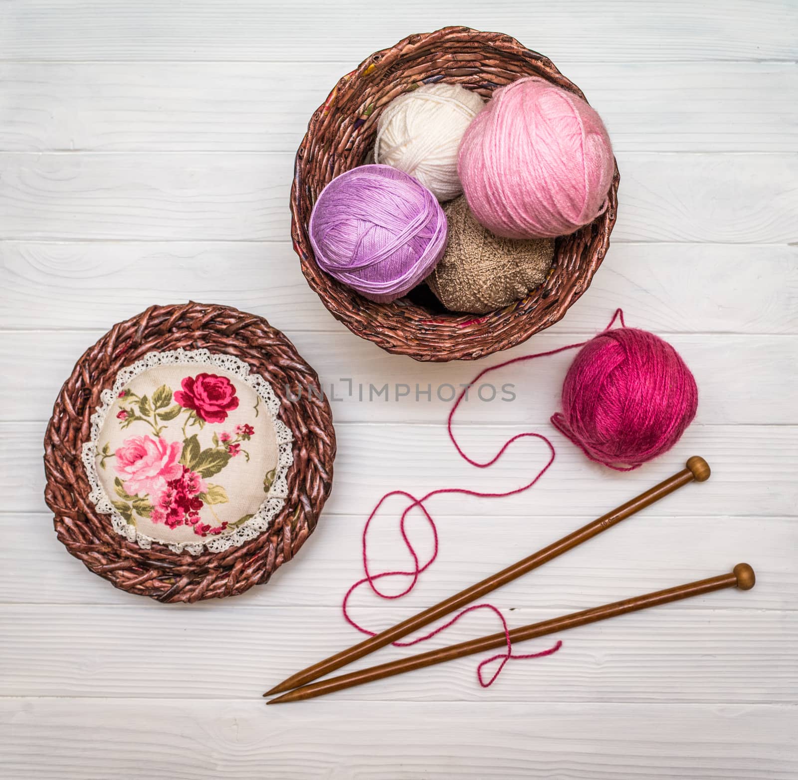 From above the colored balls of yarn in wicker basket with needles on white wooden board in Ukraine