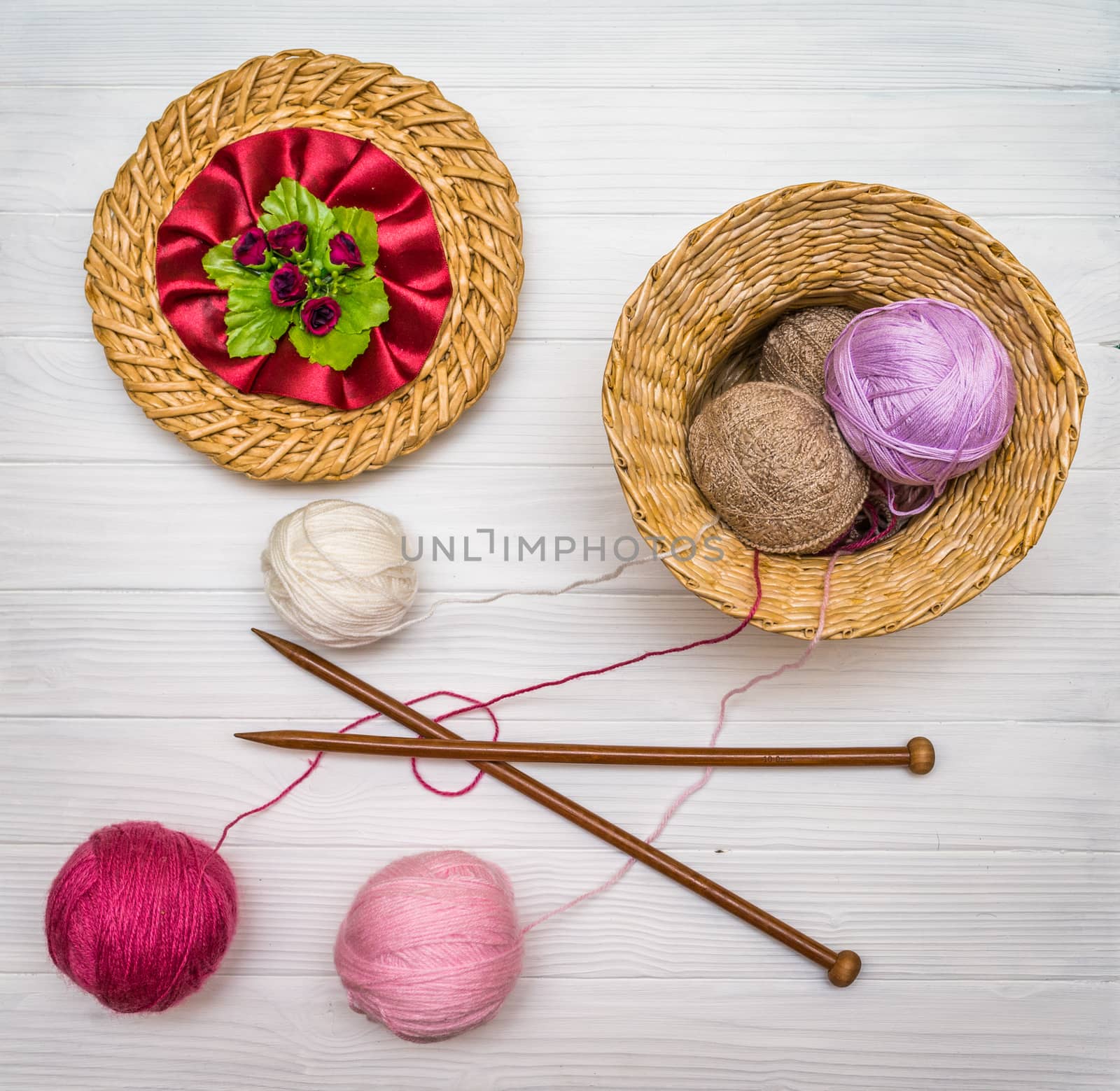 From above the colored balls of yarn in wicker basket with needles on white wooden board in Ukraine