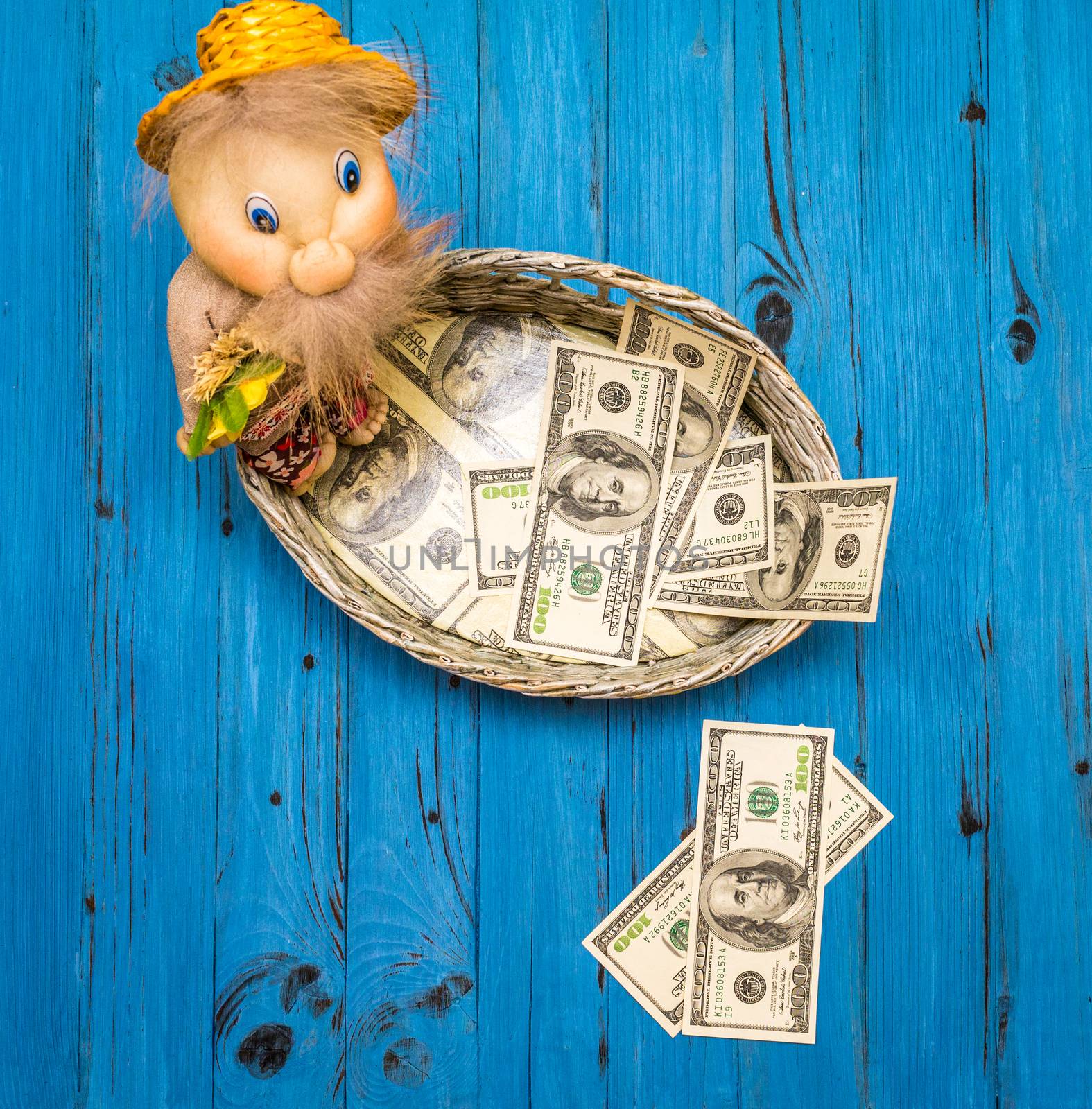From above few dollar bills in a wicker basket and two hundred dollars bills on board with traditional toy of man on a blue wooden board in Ukraine.
