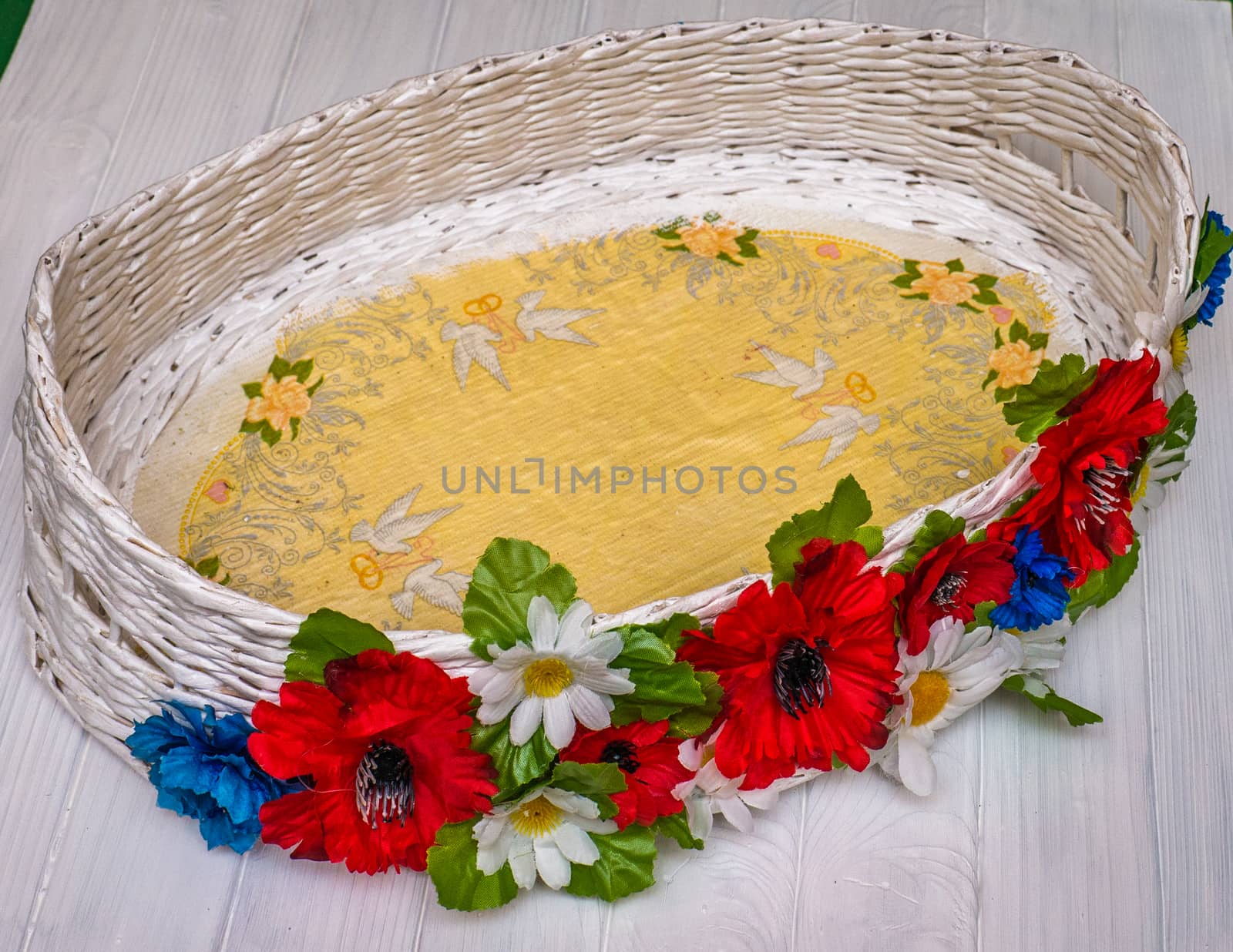 From above empty wicker basket decorated with red and white flowers on a white wooden board in Ukraine