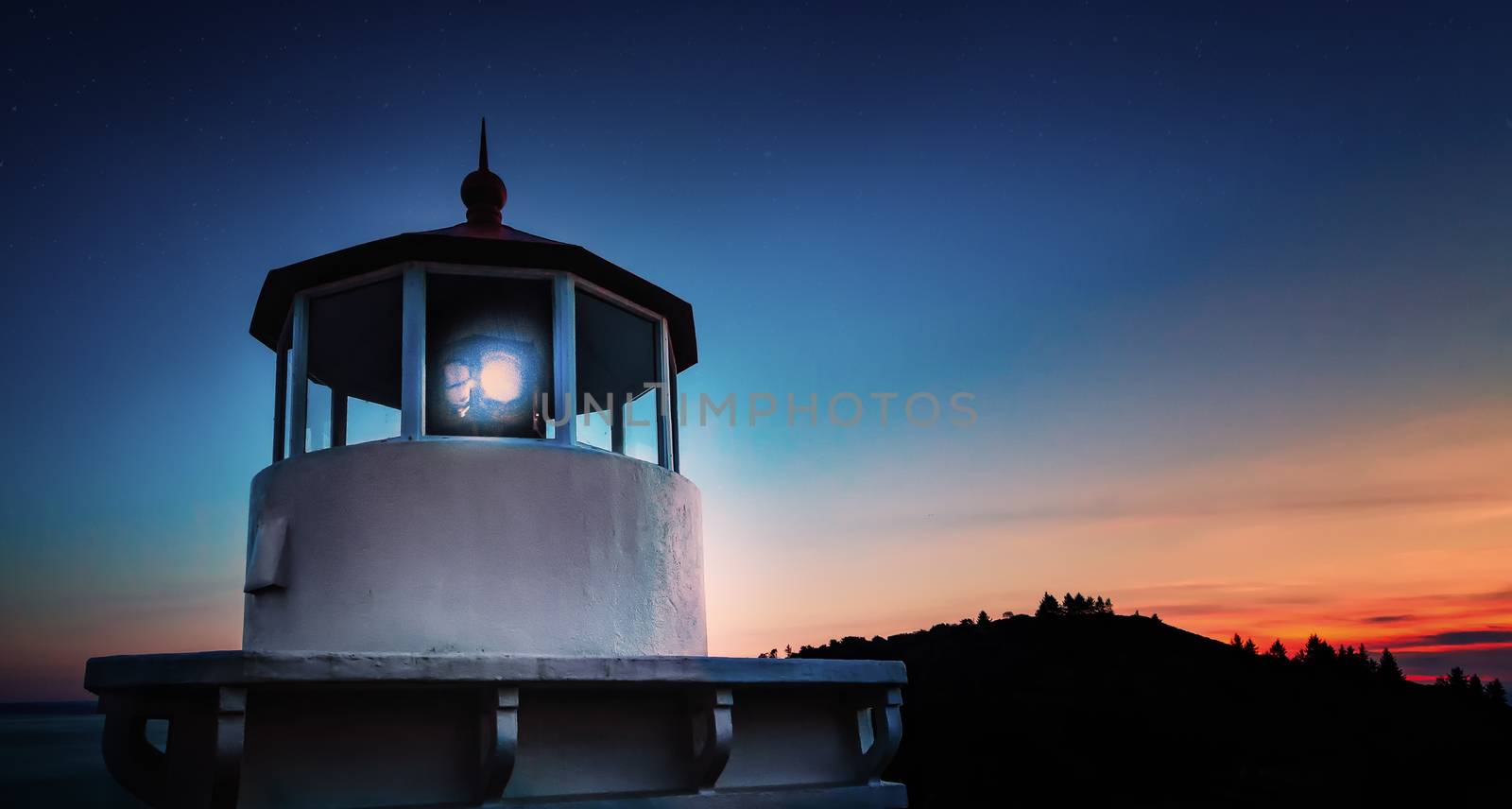 A Lighthouse shines at sunset. Color image.