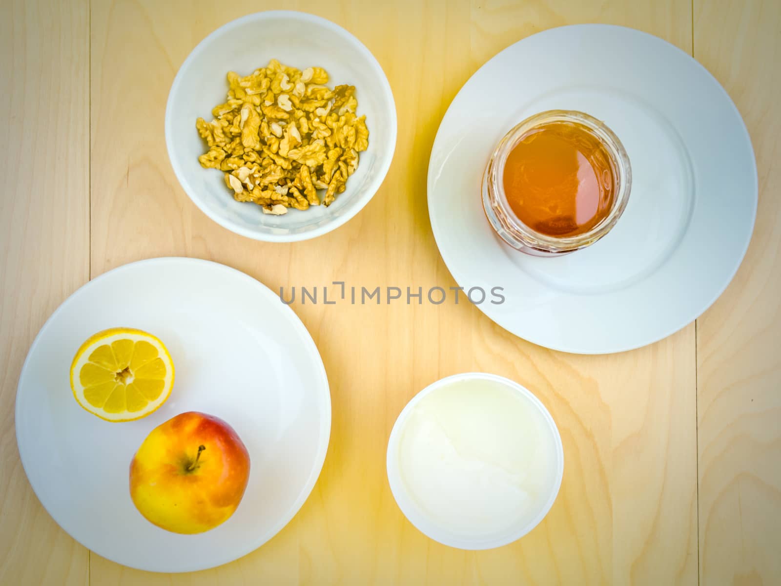 Four ingredients for a healthy and nutritious snack or smoothie, apple lemon fruit, cottage cheese, honey , shelled nuts walnuts, on plates from top view, arranged on wooden table in soft colours