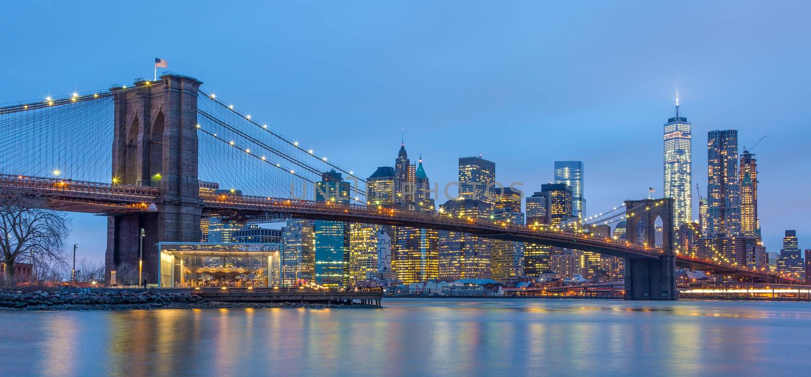 Brooklyn bridge and New York City Manhattan downtown skyline at dusk with skyscrapers illuminated over East River panorama. Panoramic composition.