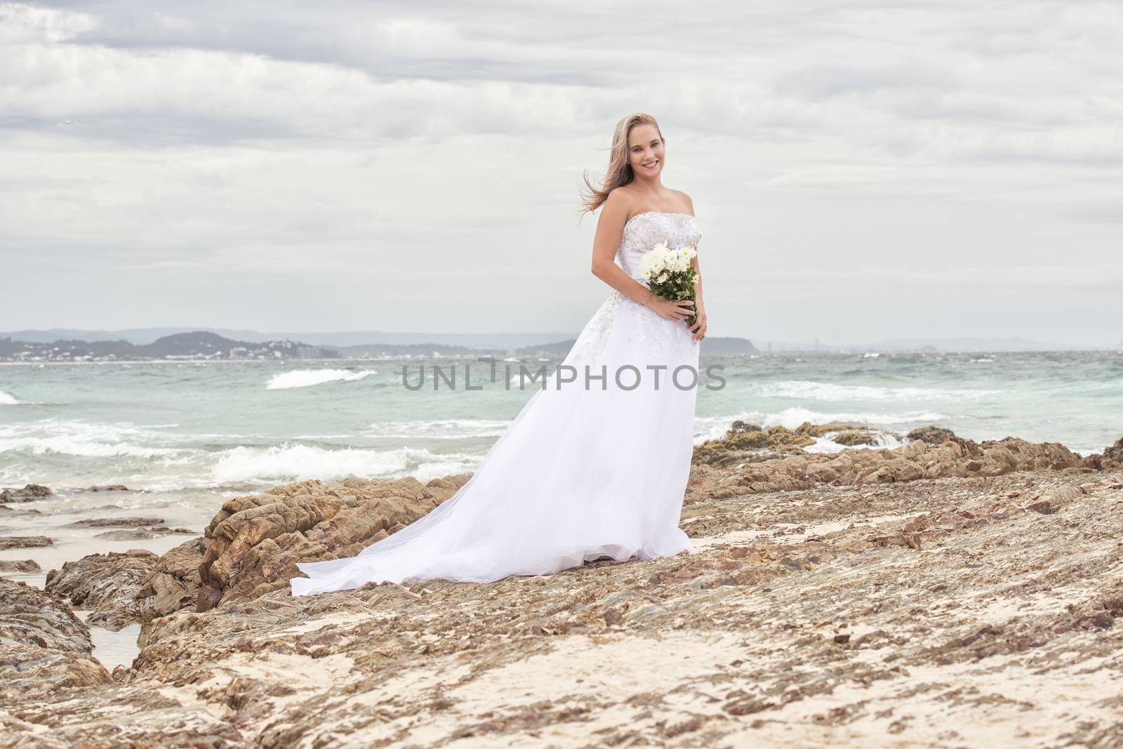 Beautiful bride at the beach with a flower bouquet.