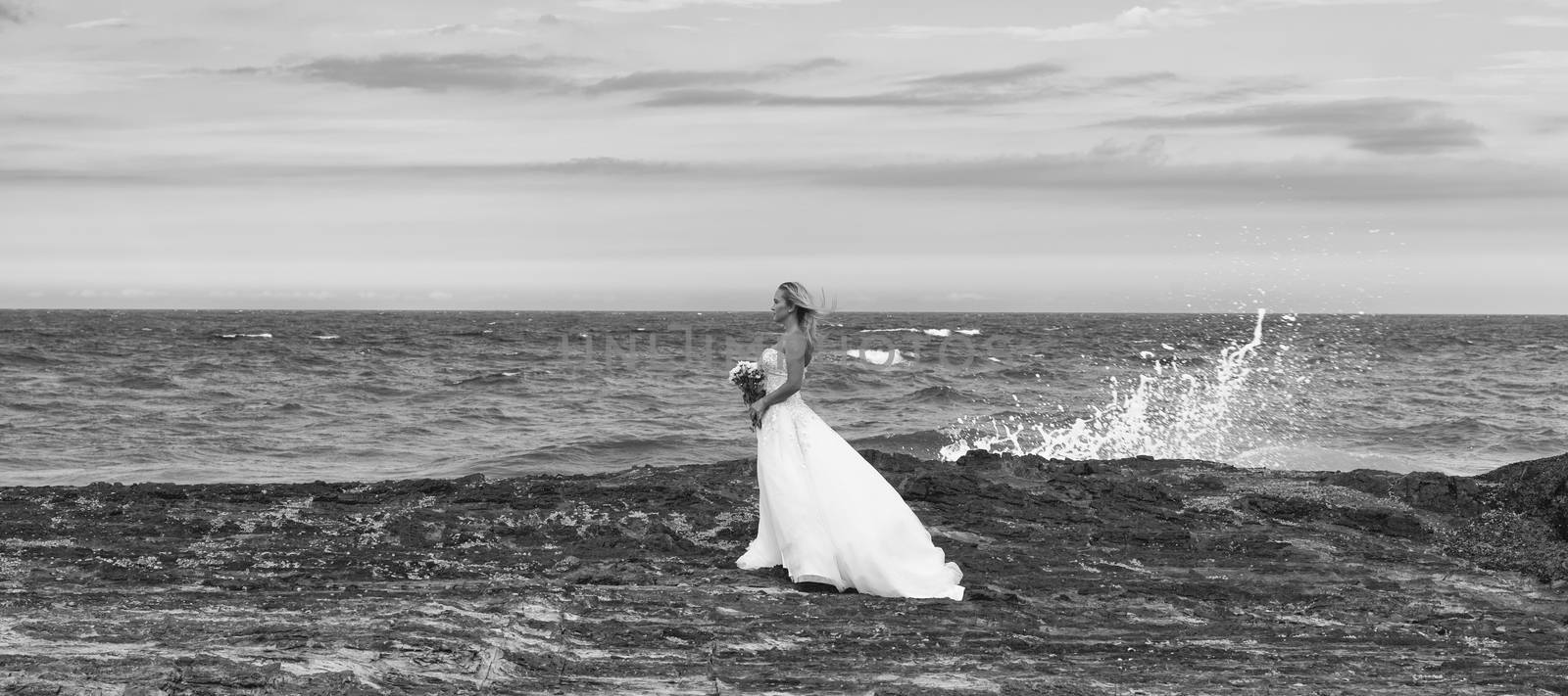 Beautiful bride at the beach with a flower bouquet.