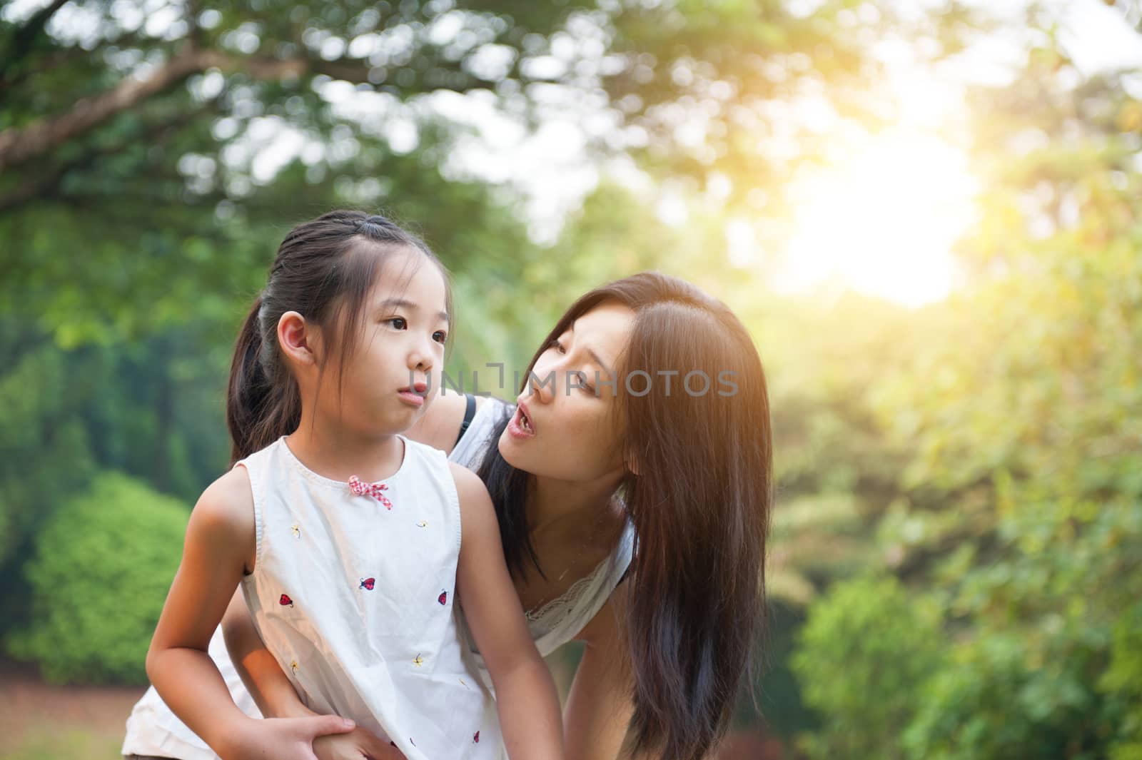 Mother embracing daughter in the park , Asian family outdoor lifestyle, morning with sun flare.