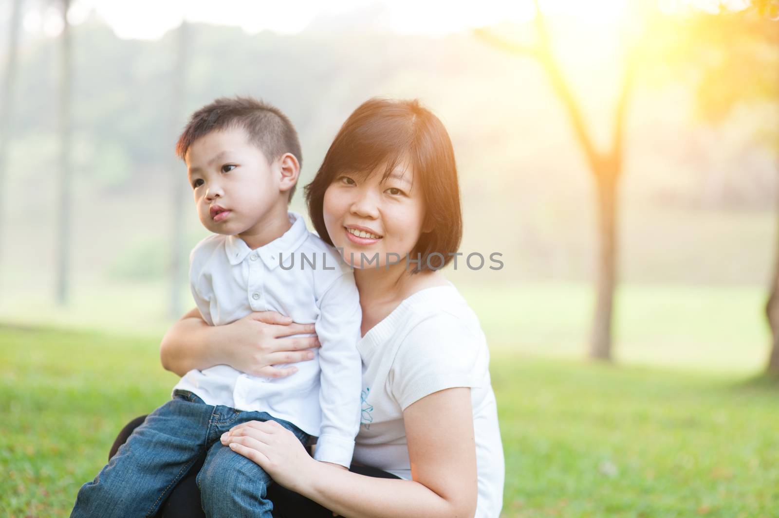 Mother hugging son in the park, Asian family outdoor lifestyle, morning with sun flare.