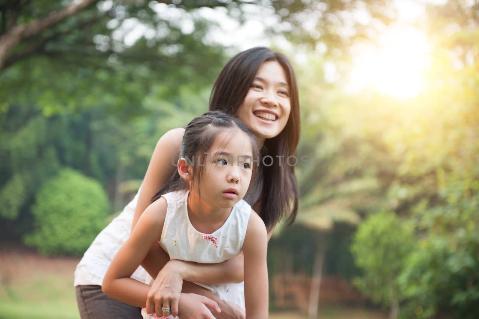 Mother hugging daughter in the park , Asian family outdoor lifestyle, morning with sun flare.