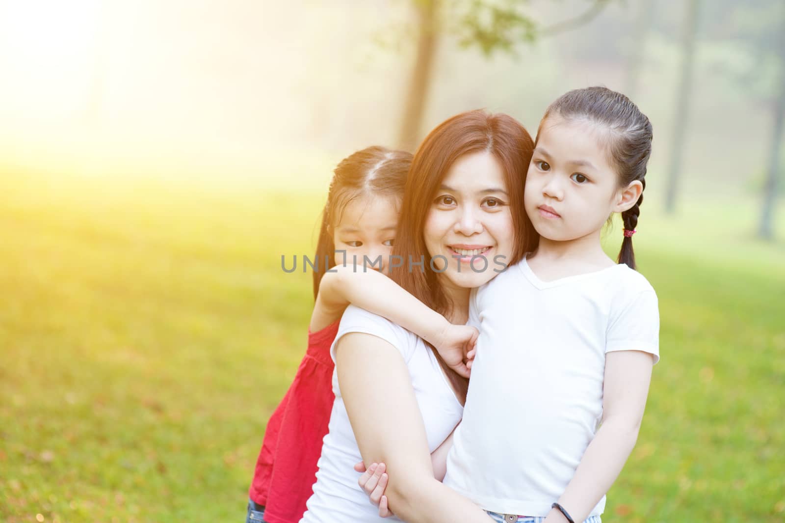 Lifestyle portrait Asian mother and daughter hugging in love at the outside in the park. Family outdoor fun, morning with sun flare.