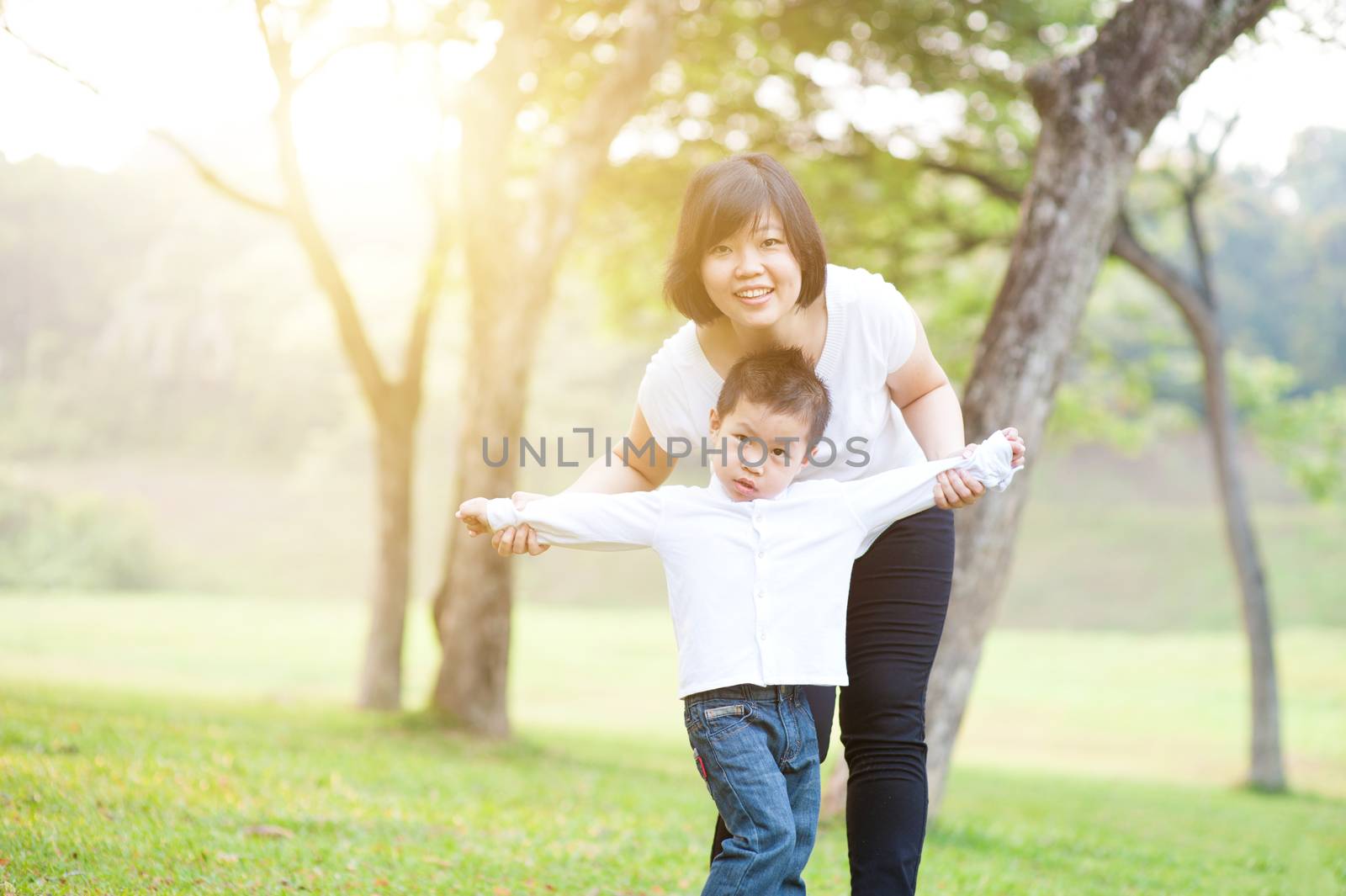 Mother and son playing in the park. Family outdoor fun, morning with sun flare.