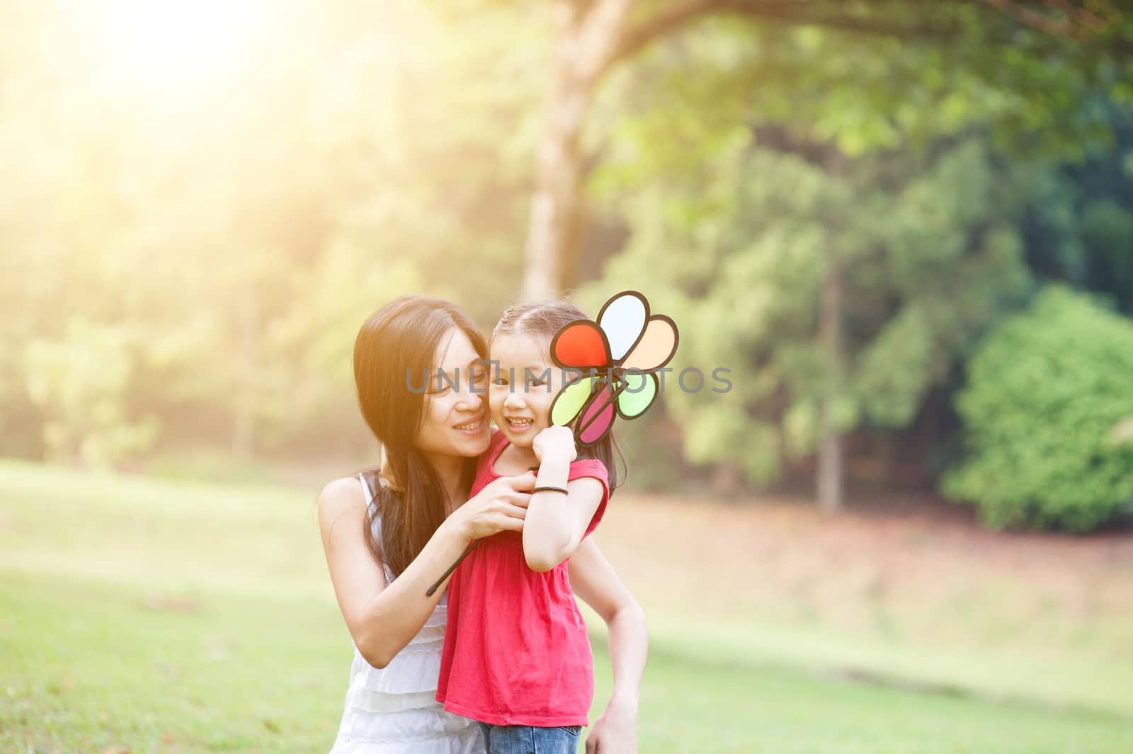 Asian mother and daughter playing in the park. Family outdoor fun, morning with sun flare.