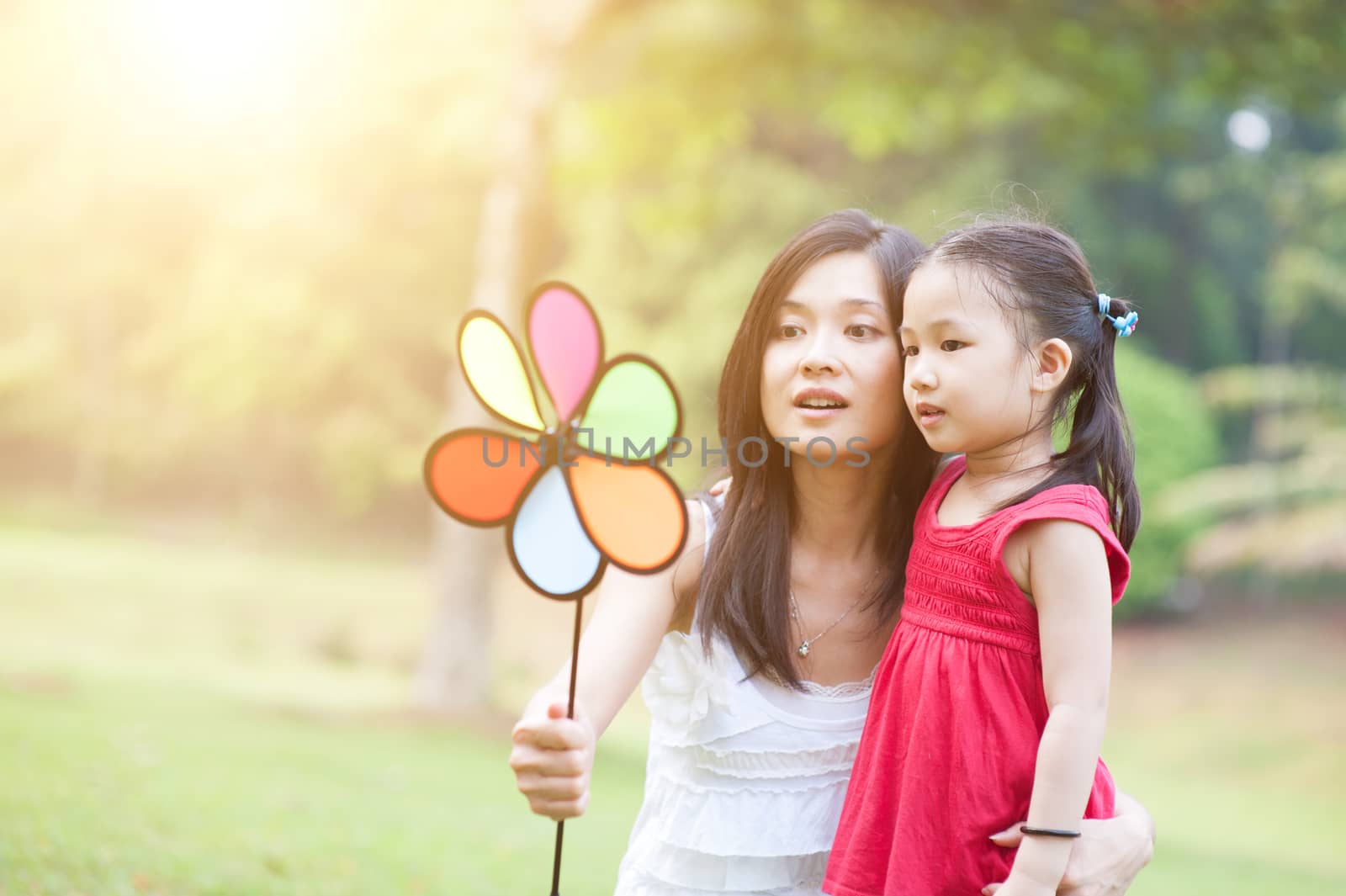 Asian mother and daughter playing in a park on a morning, with sun flare. Family outdoor fun.