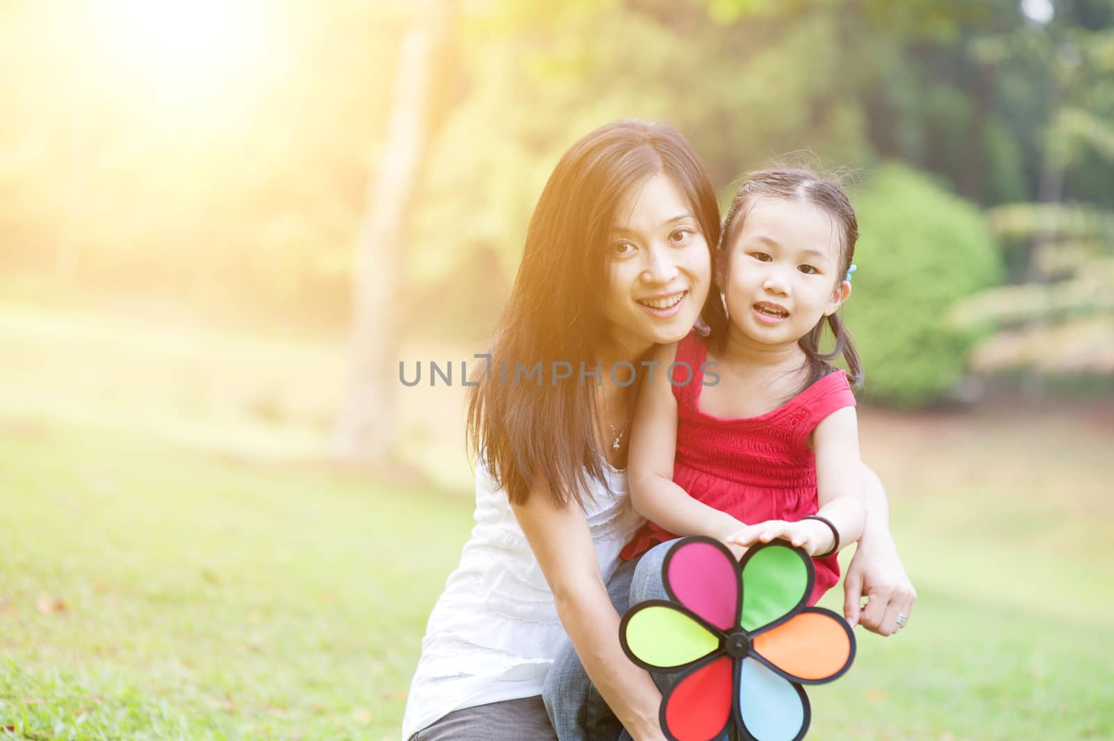 Happy mother and daughter laughing together outside, in the park. Family outdoor fun, morning with sun flare.