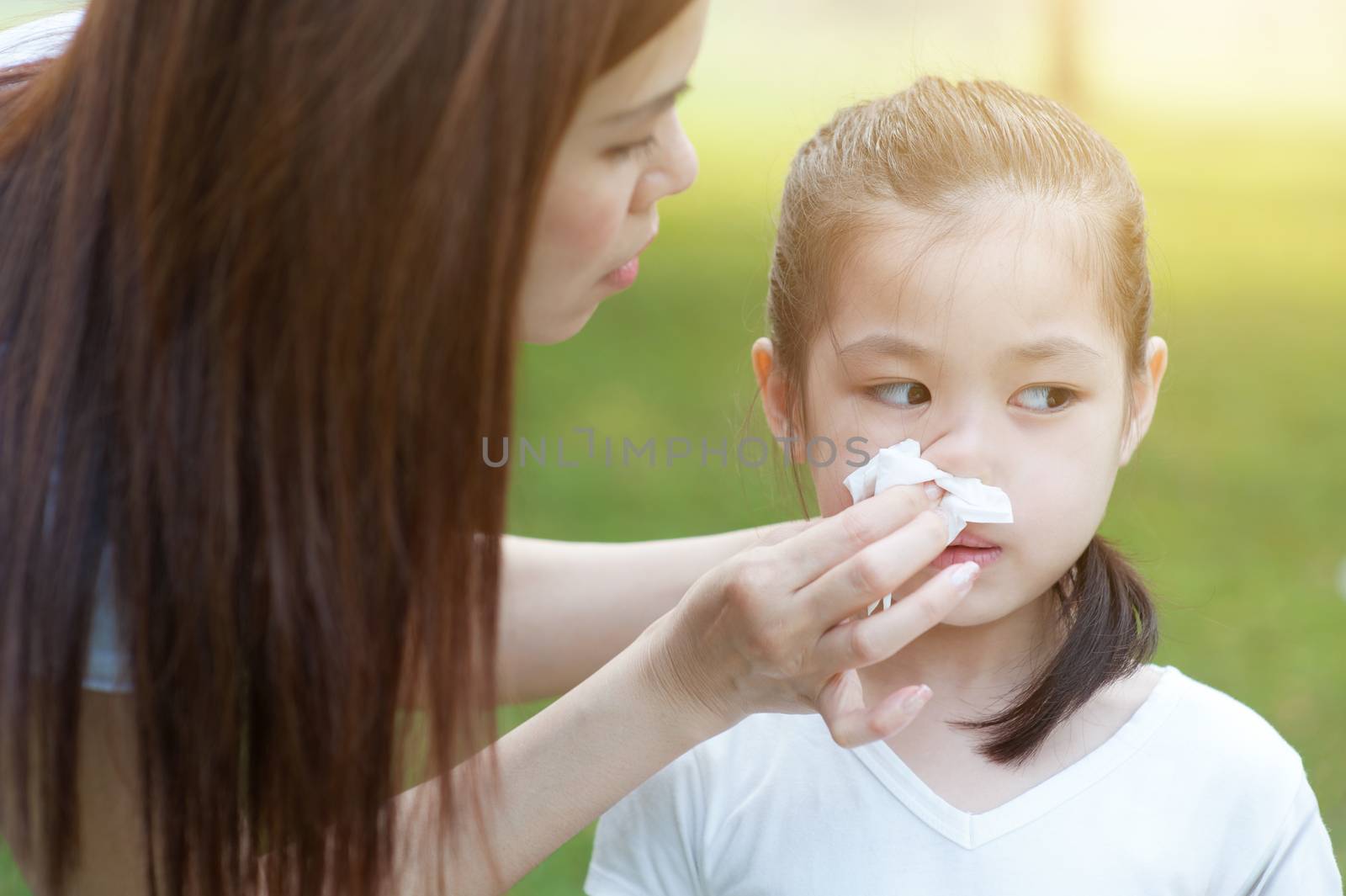 Allergy. Mother helping daughter blow her nose at outside, in the park. Family outdoor lifestyle.