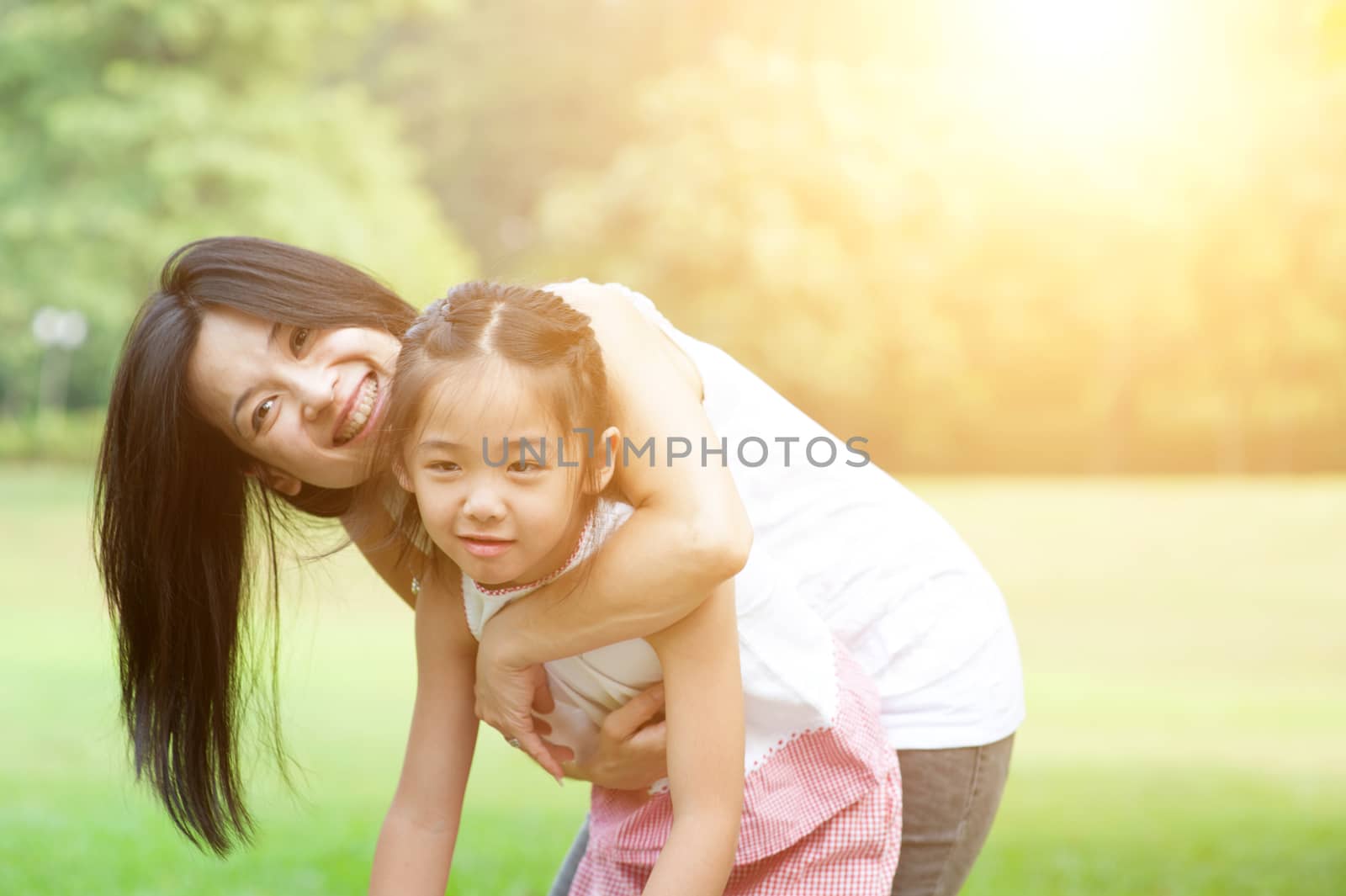 Mother and daughter hugging in love playing in the park. Mothers Day. Family outdoor fun, morning with sun flare.