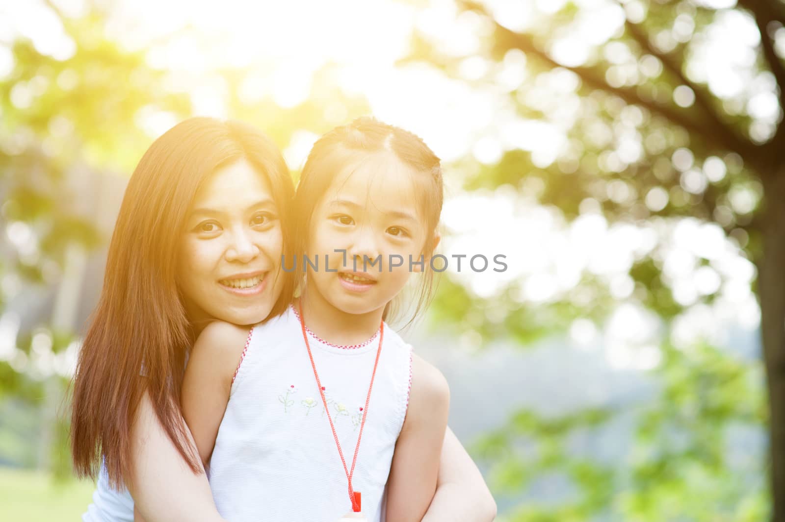 Mother and child are hugging and having fun outdoor in nature - photo with sun flare.