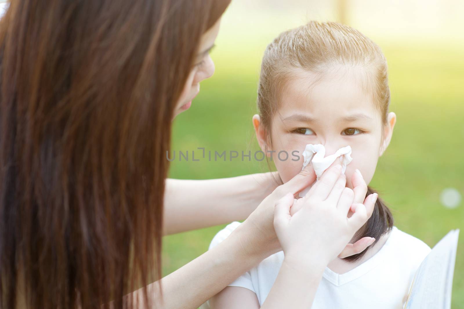 Allergy. Mother and little girl blowing nose at outside, in the park. Family outdoor lifestyle.