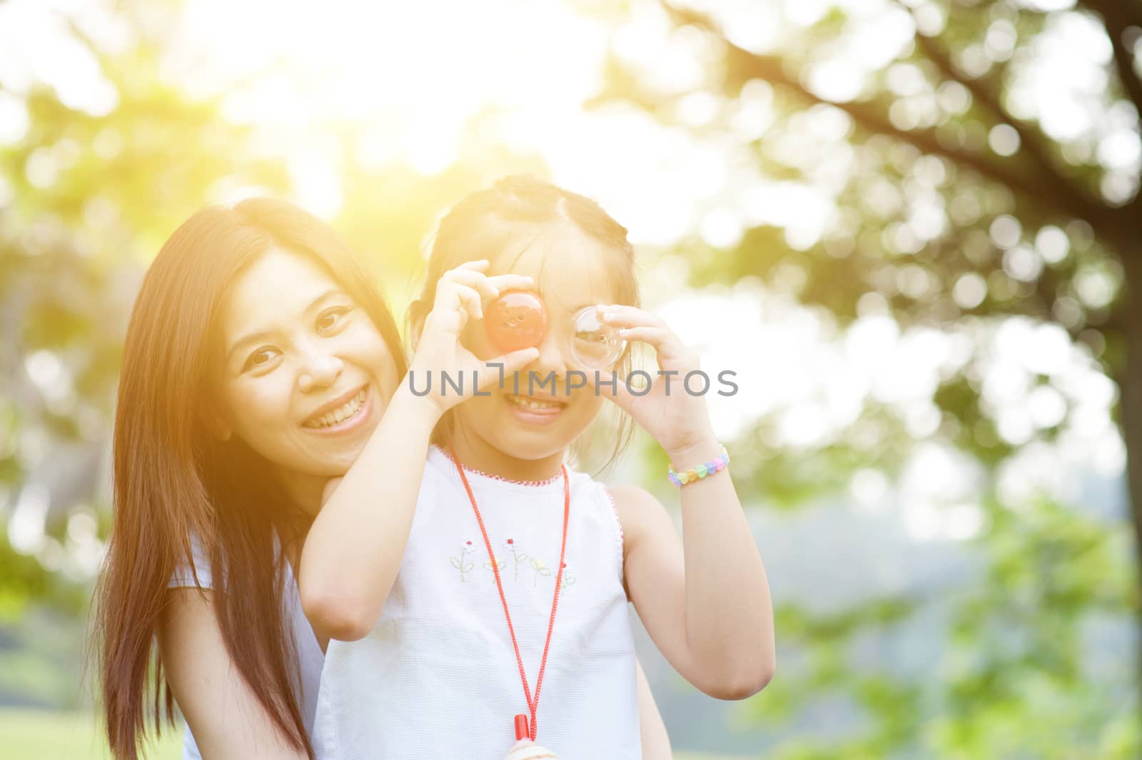 Mother and daughter smiling in a park on a morning, with sun flare.