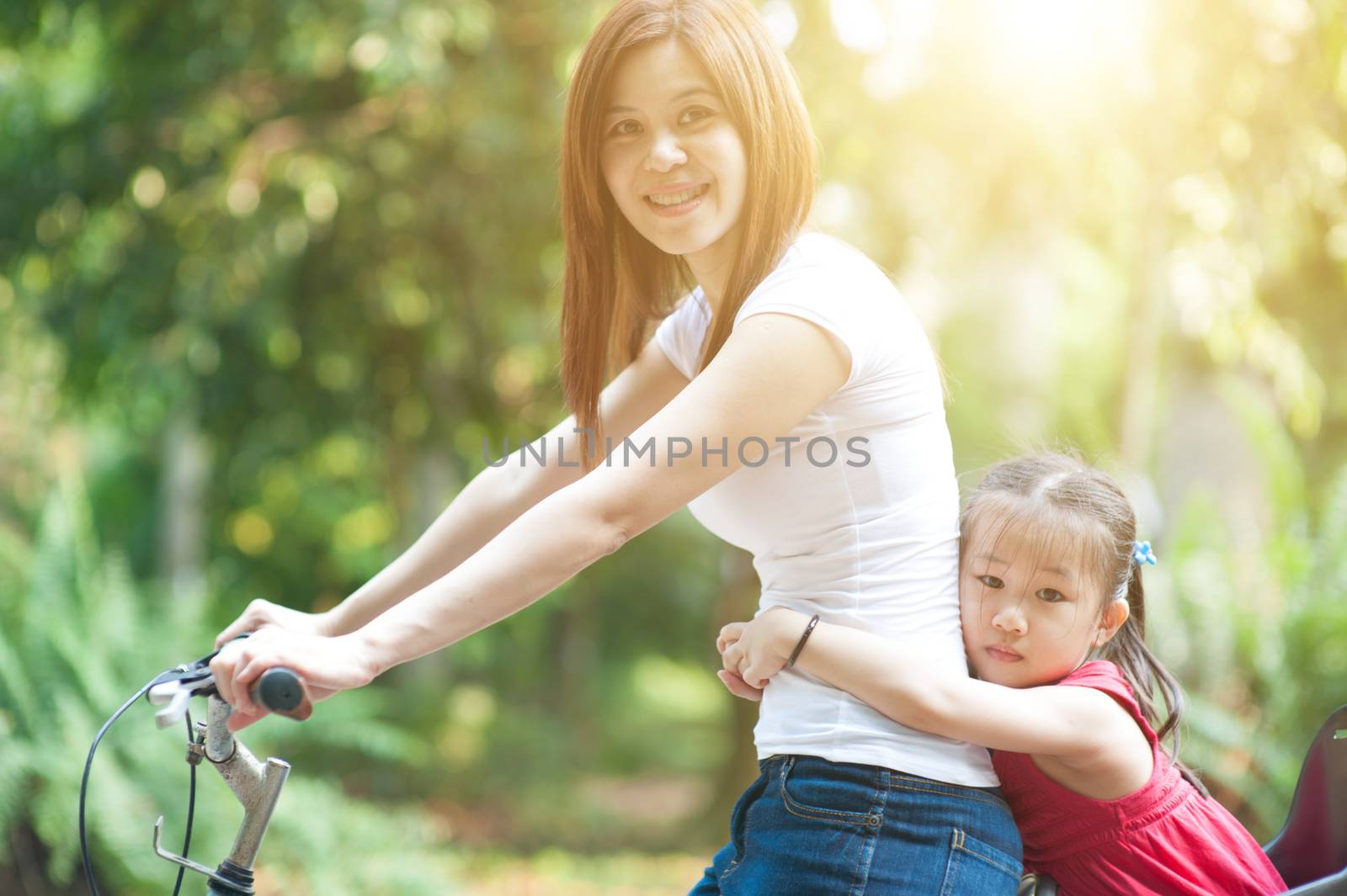 Mother and daughter riding bicycle in garden park, Asian family outdoor fun activity.