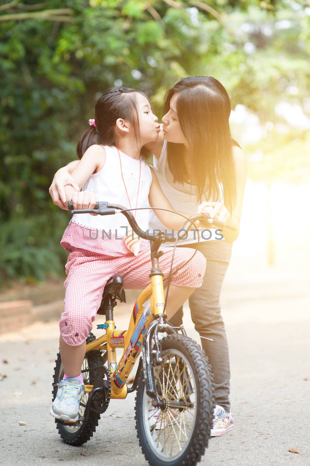 Child riding bike and giving kiss to mother, outdoor park. by szefei