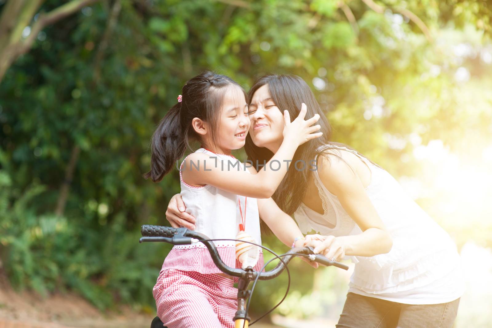 Little girl biking in the park, mother giving a goodbye kiss , Asian family outdoor fun activity.