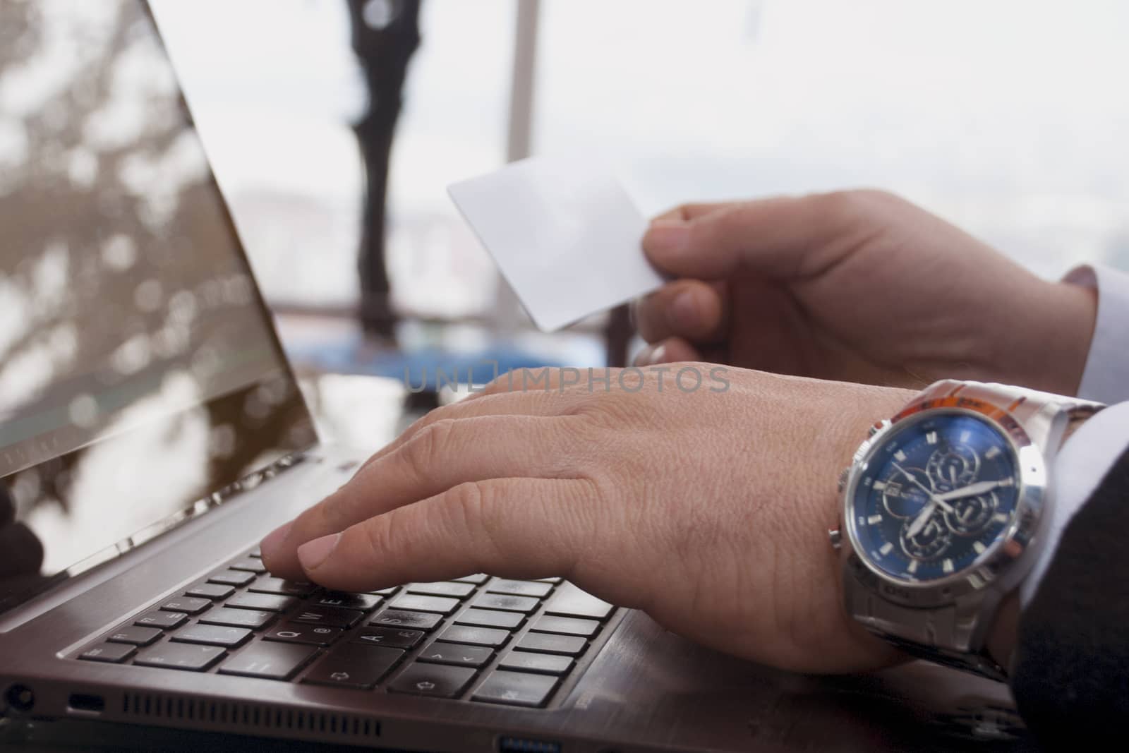 The rear view of male hands holding a credit card by typing on laptop computers while sitting across the image.