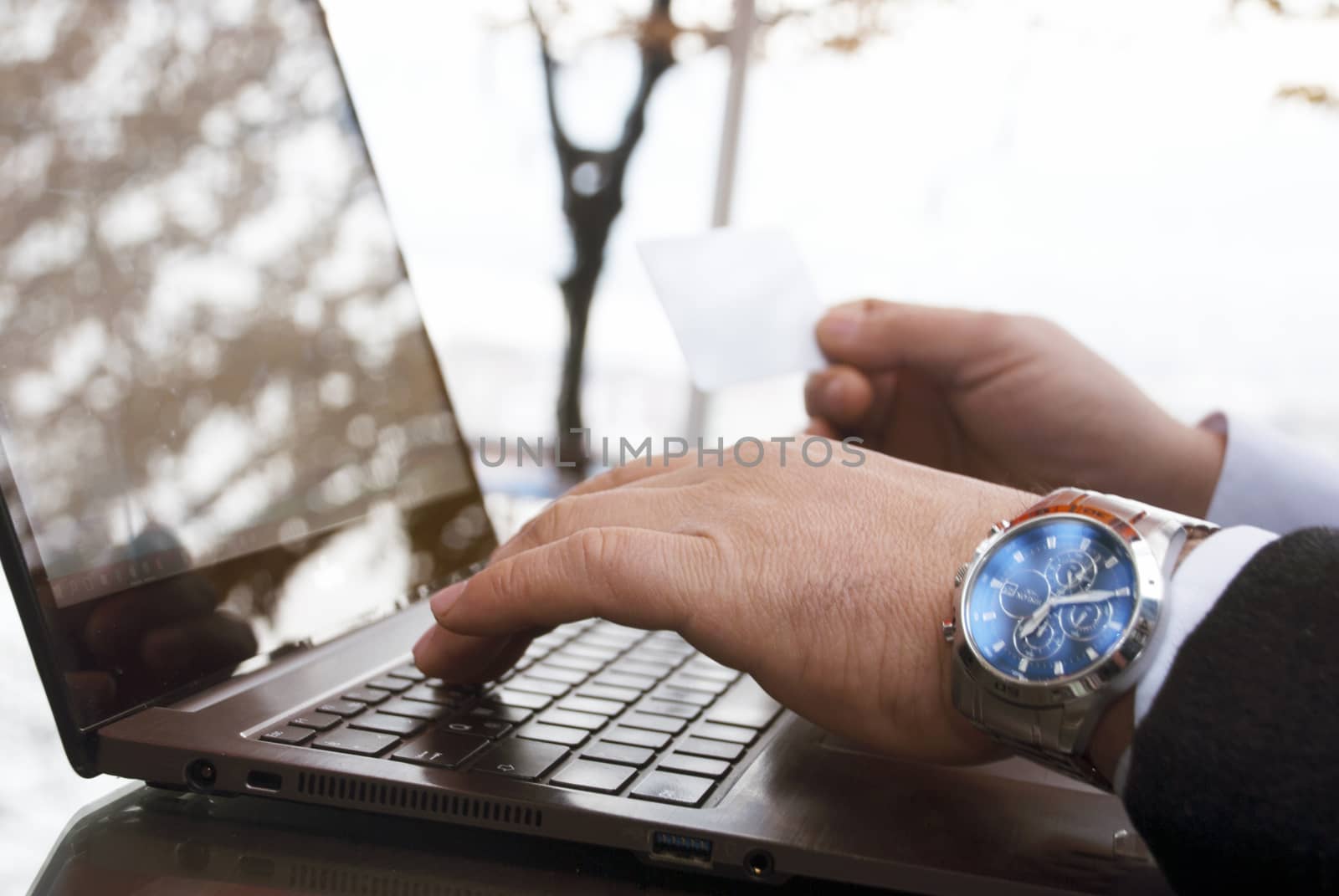 The rear view of male hands holding a credit card by typing on laptop computers while sitting across the image.