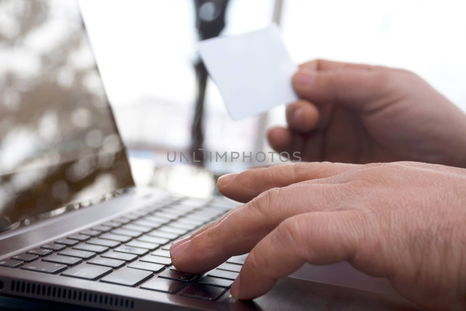 The rear view of male hands holding a credit card by typing on laptop computers while sitting across the image.