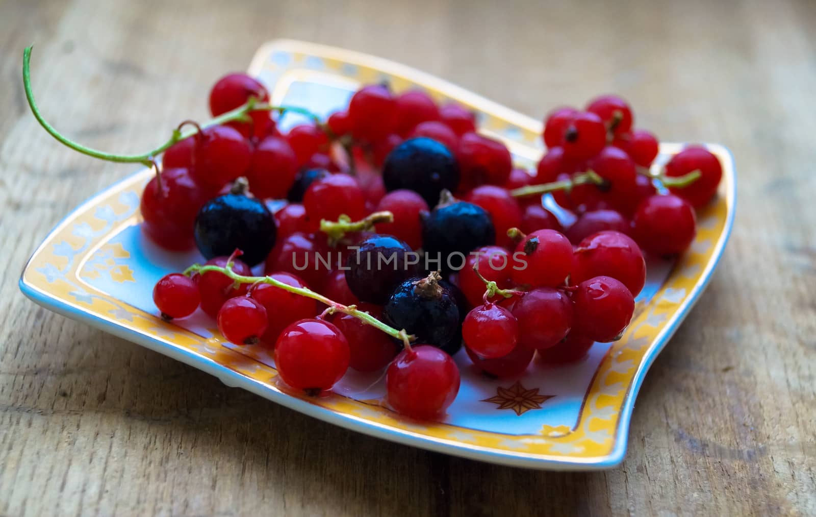 currant berries on a plate on a wooden background by Oleczka11