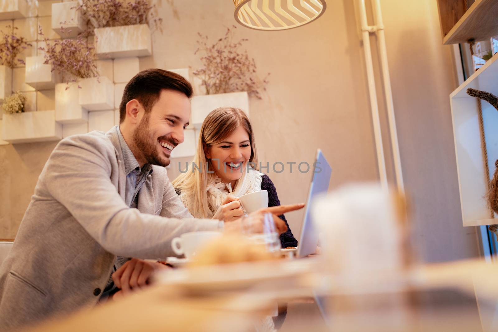Two beautiful young smiling businesspeople sitting at cafe, talking and drinking coffee.