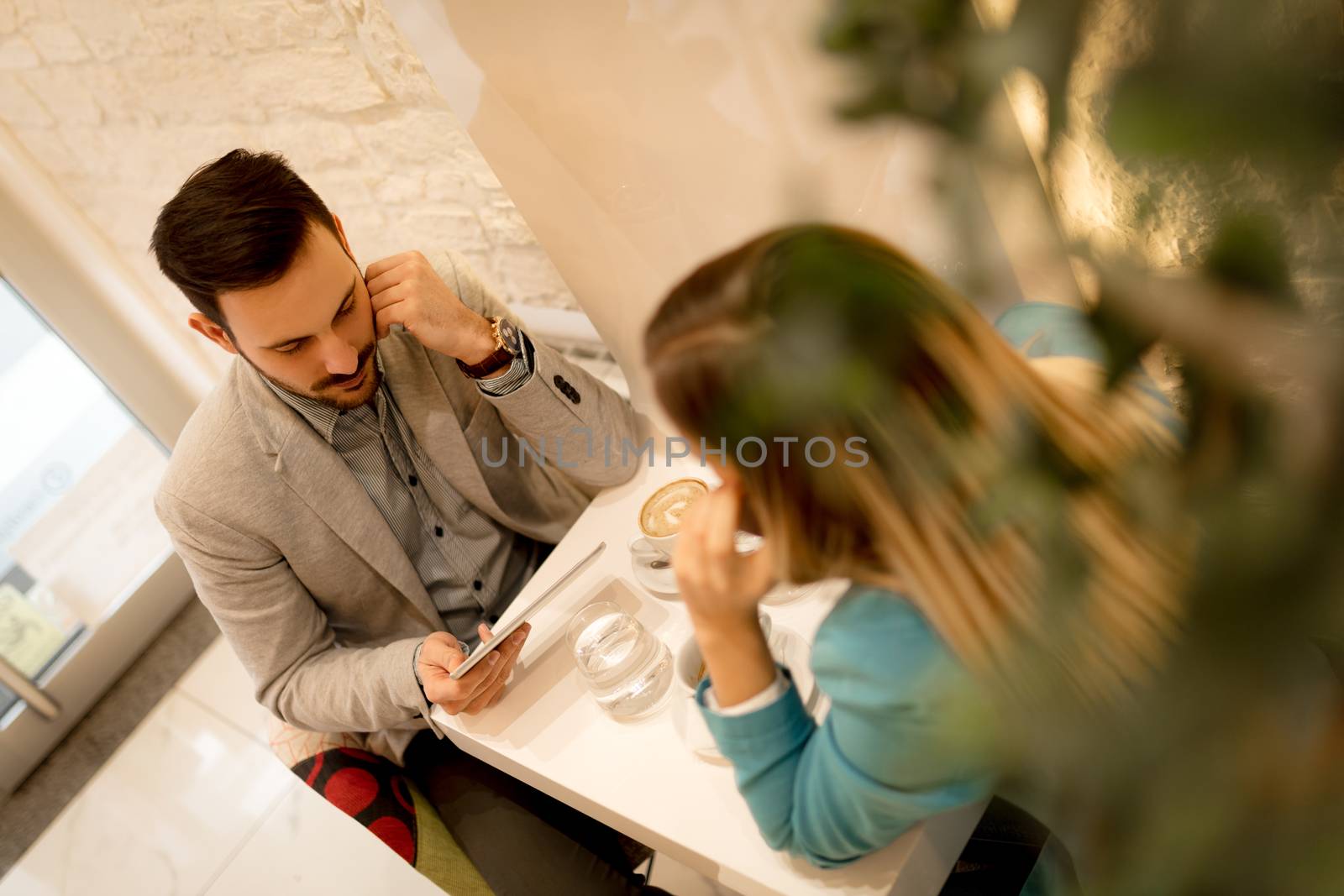 Young businesspeople on a break in a cafe. Pensive man working at tablet. Woman using smart phone. Selective focus. Focus on businessman.