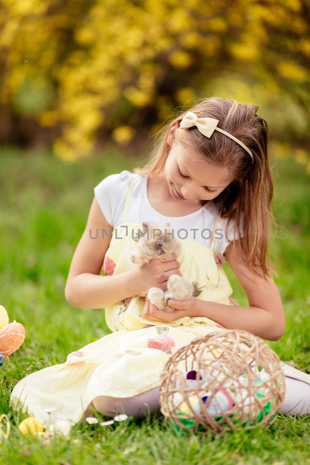 Beautiful smiling little girl holding cute bunny and sitting on the grass in spring holidays. 