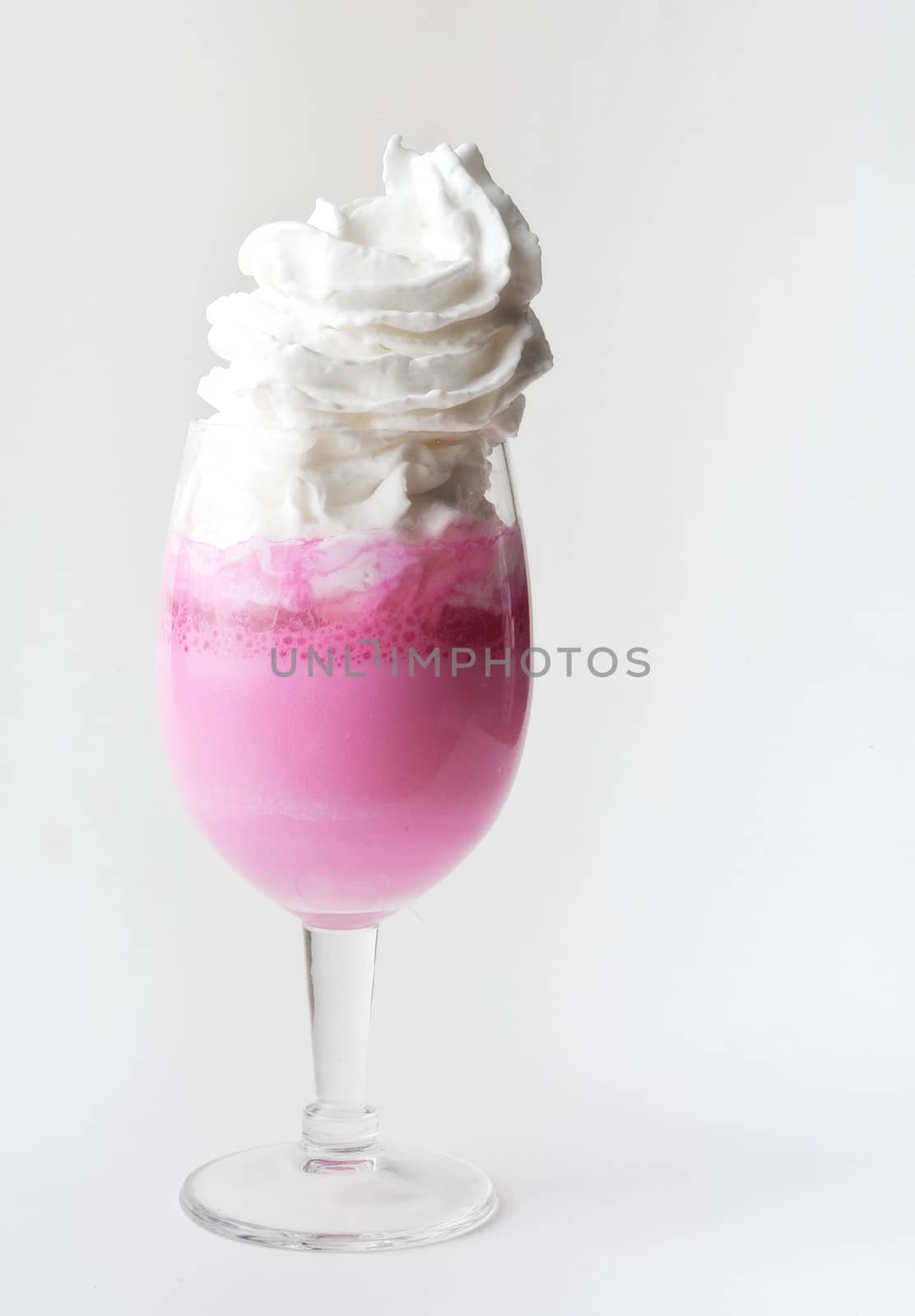A pink, frothy drink in a glass with whipped cream topping and isolated white background