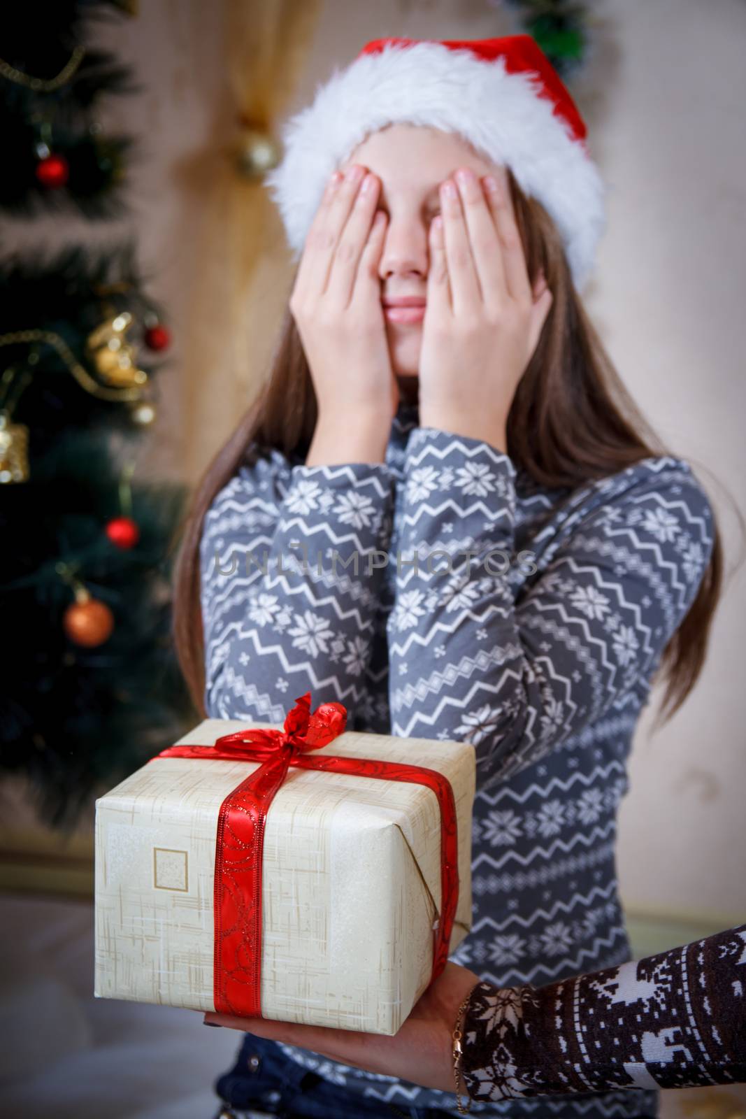 Girl closed eyes with hands in anticipation of Christmas gift, focus on gift