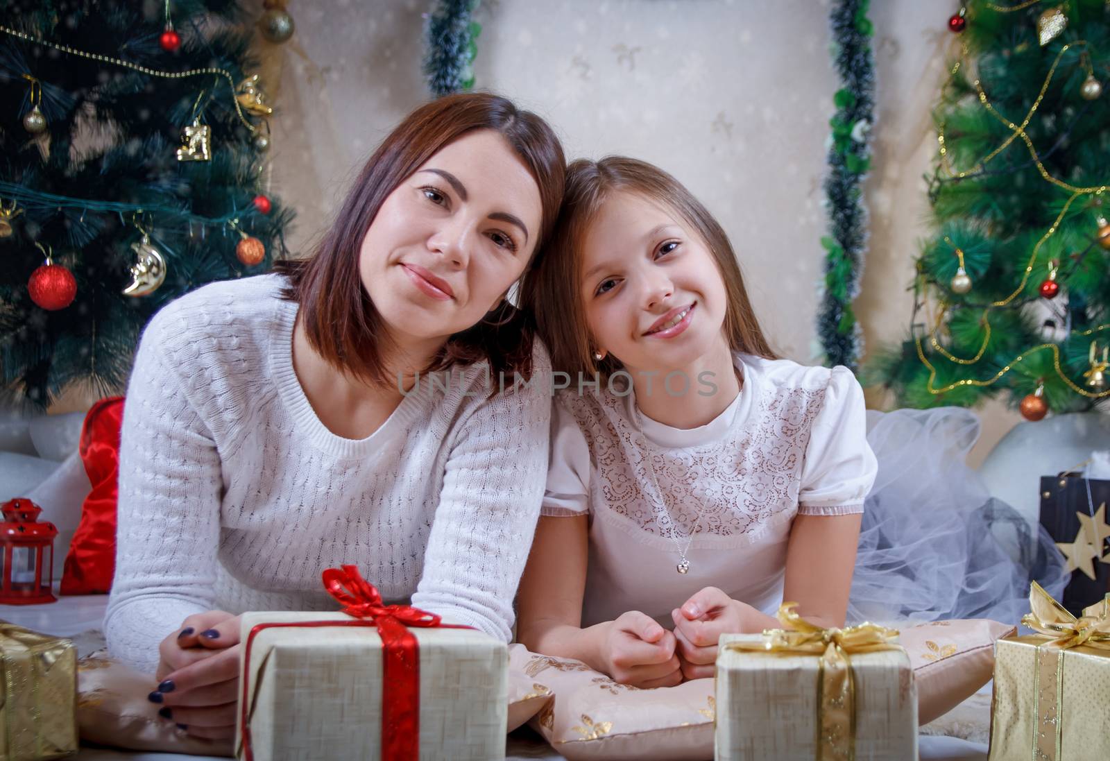 Mother and daughter lying under Christmas tree with gifts