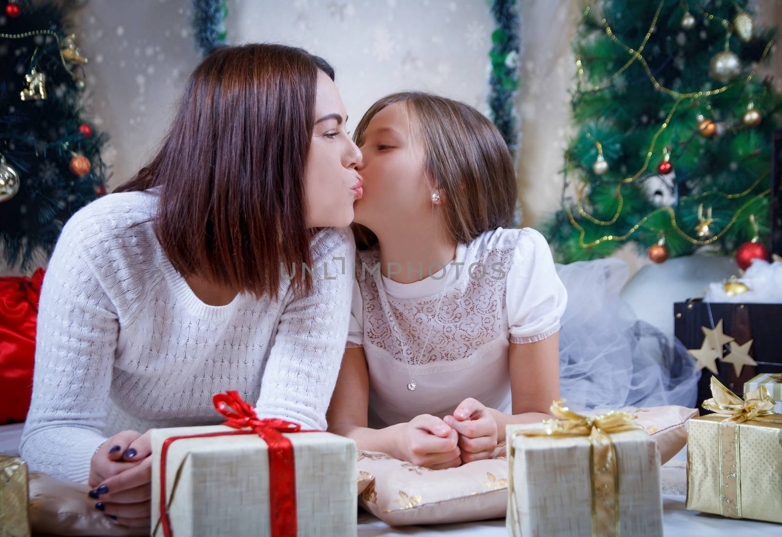 Mother kissing daughter on cheek under Christmas tree 