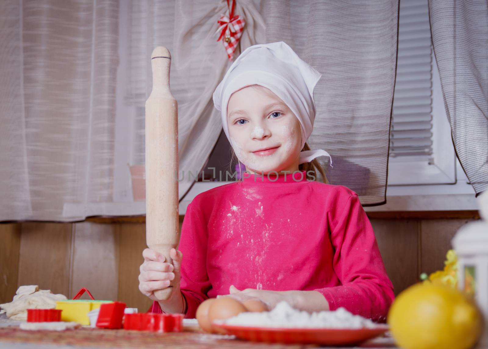 Girl making dough with rolling pin at kitchen