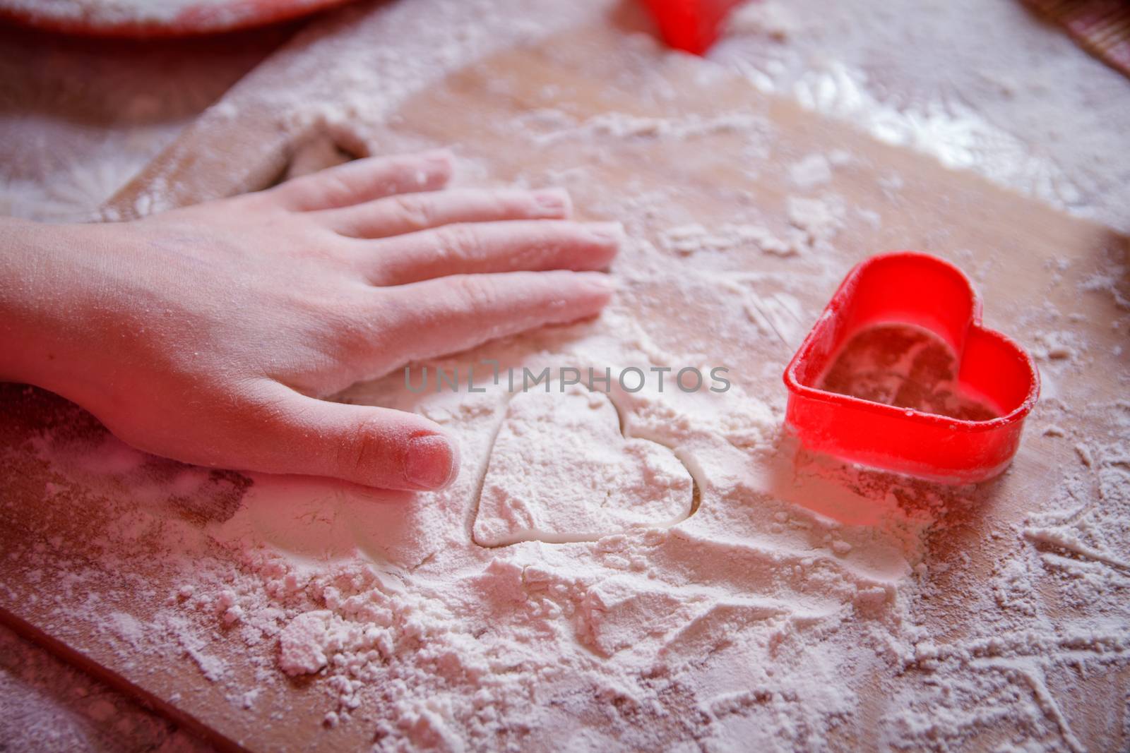 Girl hand on wooden board making heart shape on flour