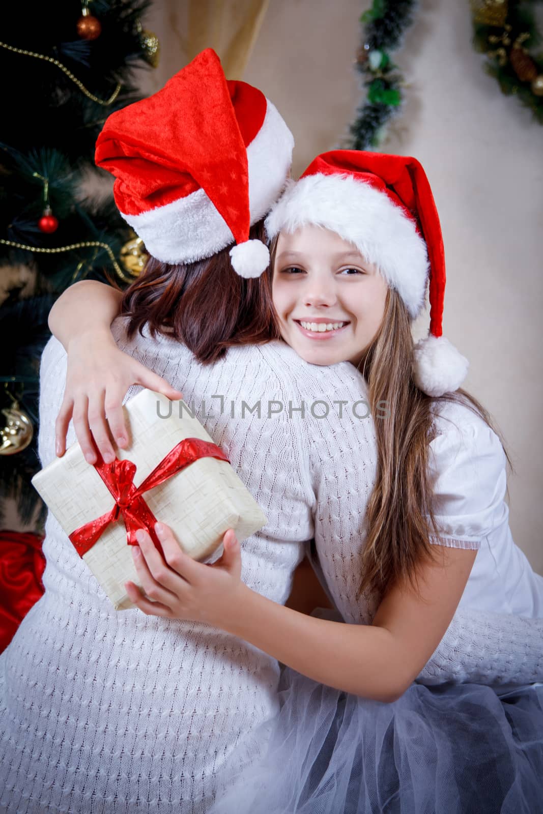 Girl in cap holding Christmas gift and hugging mother