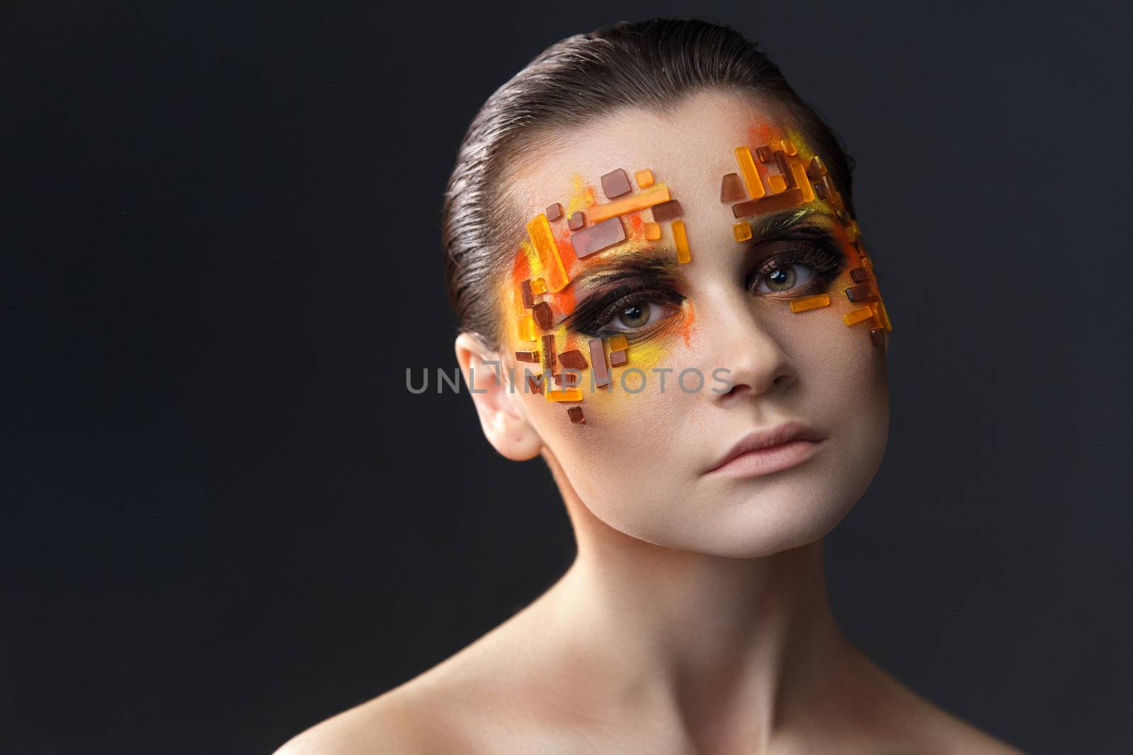 Portrait of a girl with an original make-up. Beauty close-up with orange and red rhinestones on a face of the model