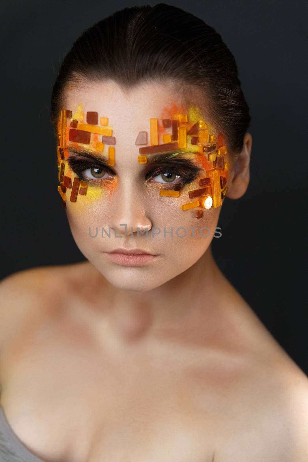 Portrait of a girl with an original make-up. Beauty close-up with orange and red rhinestones on a face of the model