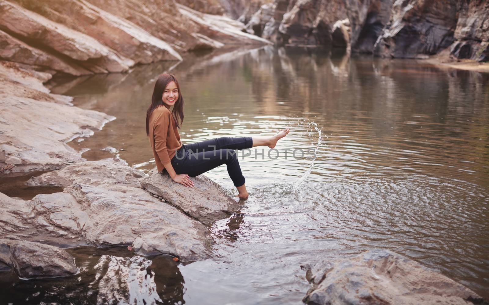 Young woman on a river bank playing with water by nopparats