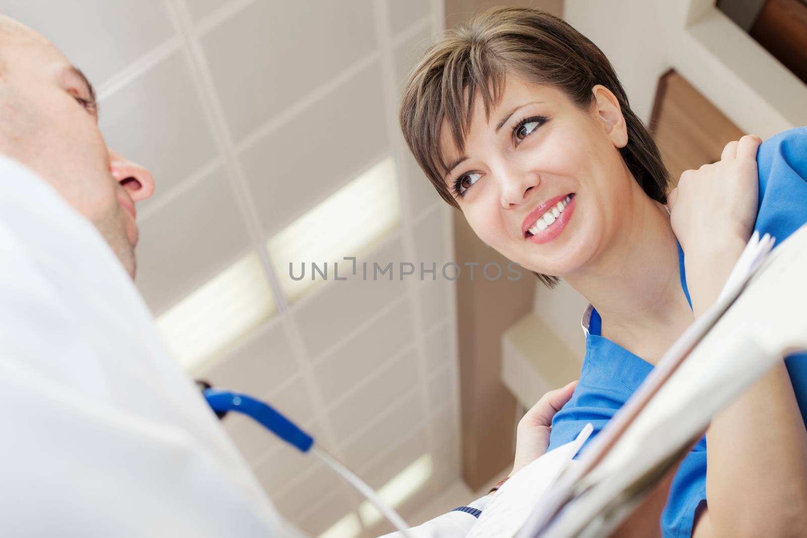 A young beautiful female patient, pointing with hand to her neck, back or shoulder is being consult by a doctor in hospital.