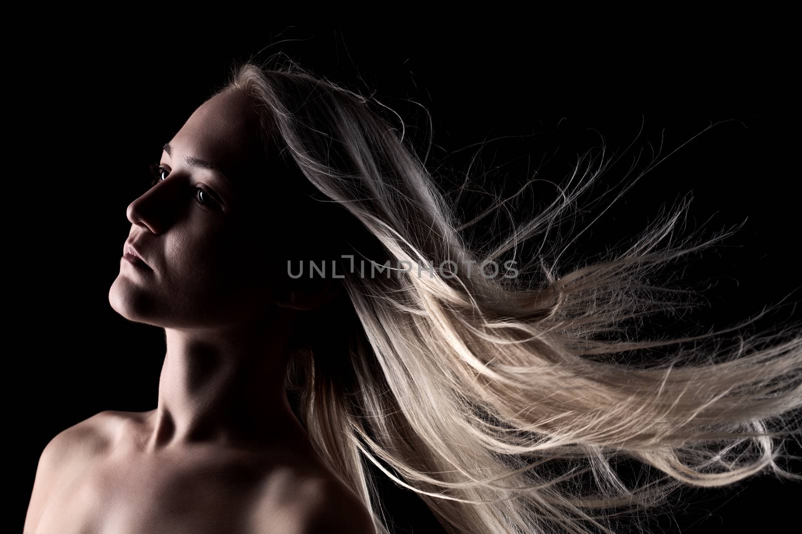 portrait of a blond girl with windy hair, on black background